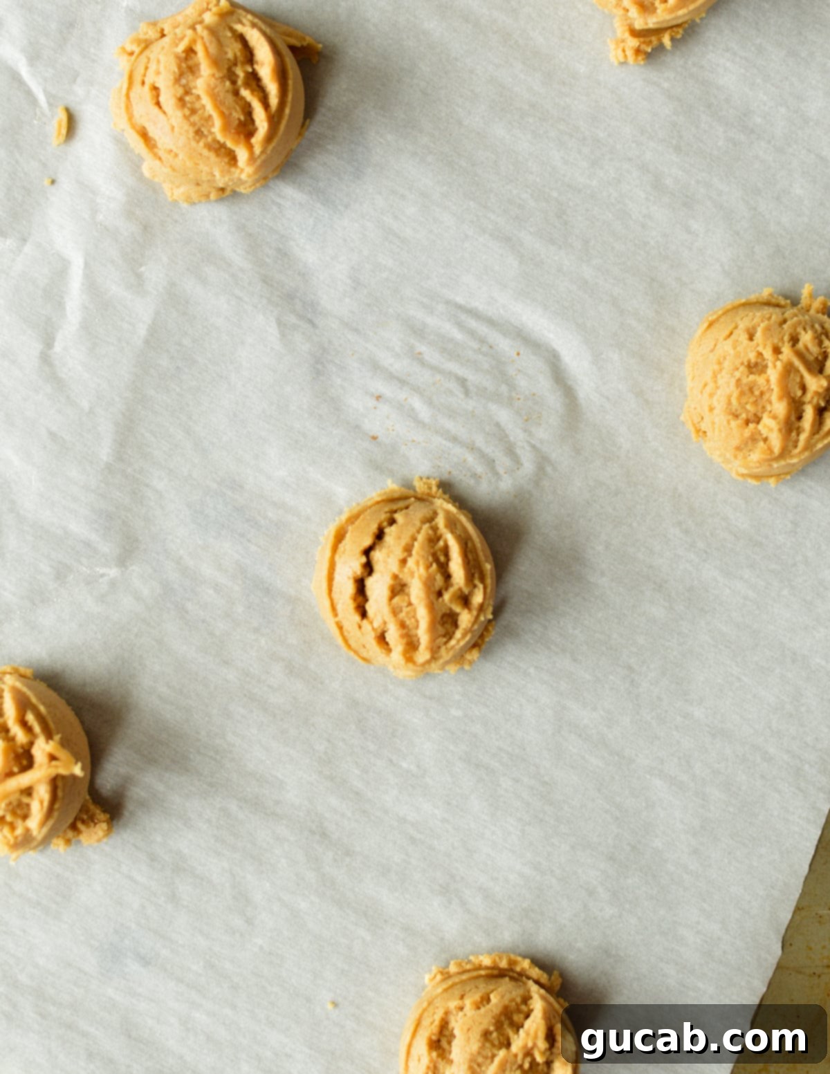 peanut butter cookie dough balls neatly arranged on a parchment-lined sheet pan.