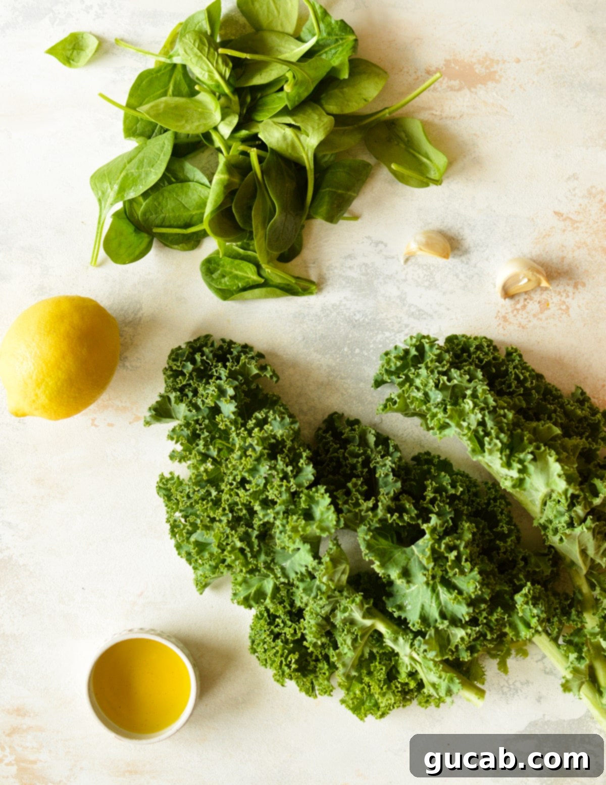 Fresh spinach, curly kale, a bright yellow lemon, and plump garlic cloves laid out as key ingredients for a healthy sauteed greens recipe.