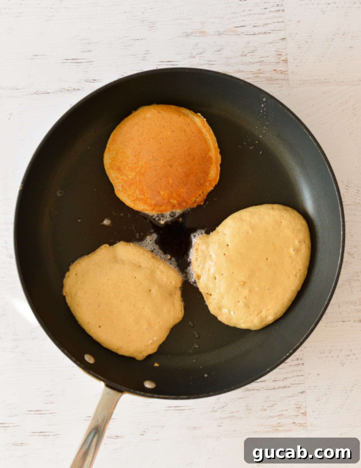 Light and Fluffy Oat Flour Pancakes 8 Oat flour pancakes cooking in a hot nonstick skillet, showing bubbles forming on the surface.