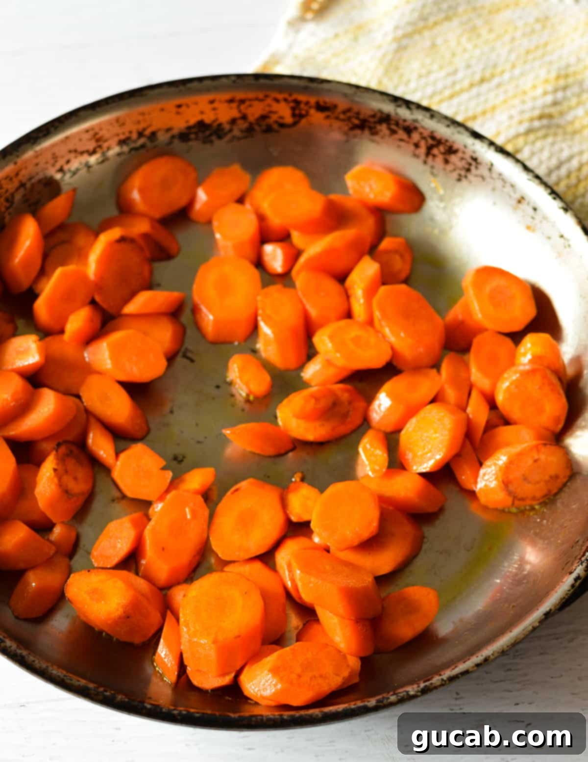 carrots being sautéed in a large stainless steel skillet over medium-high heat, showing their vibrant color and a slight char.