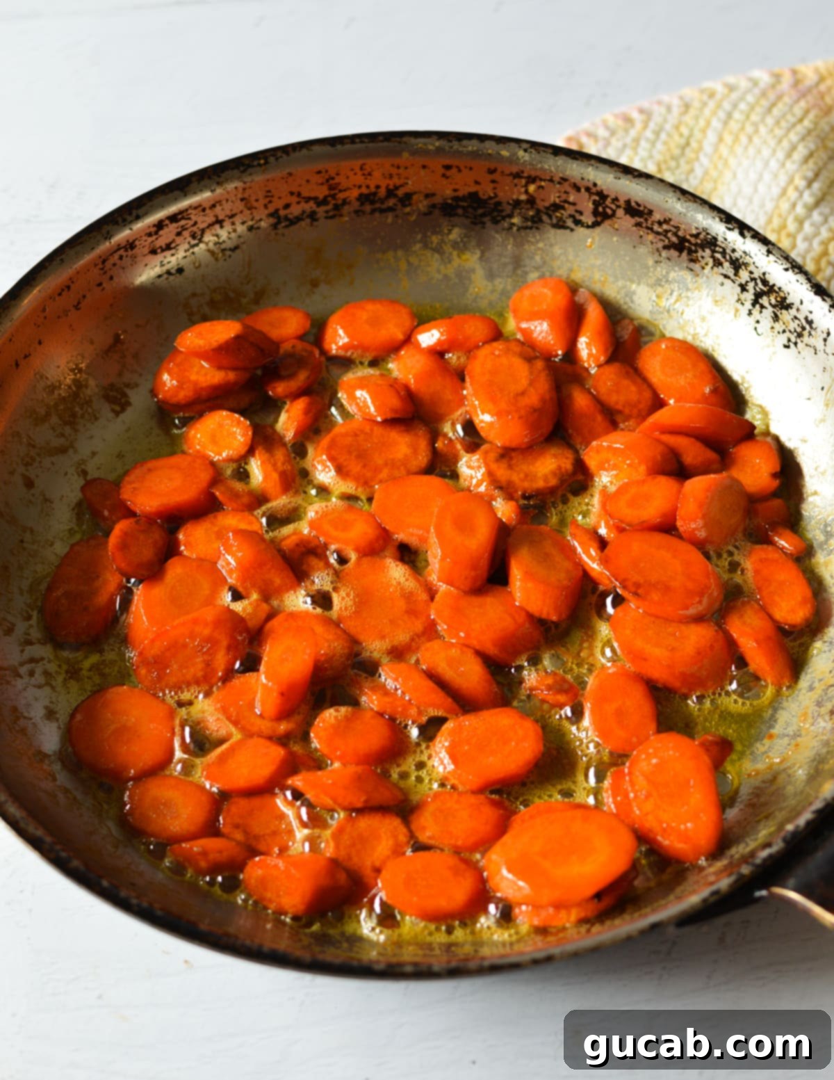maple glazed carrots simmering in a skillet, coated in a thick, shiny brown sugar and maple syrup glaze, with steam rising.