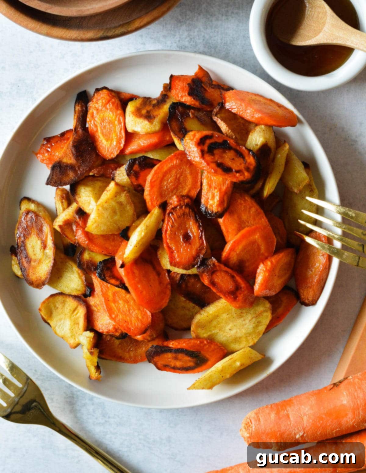 A plate of honey roasted carrots and parsnips with a gold fork next to it, showcasing their golden-brown caramelization.
