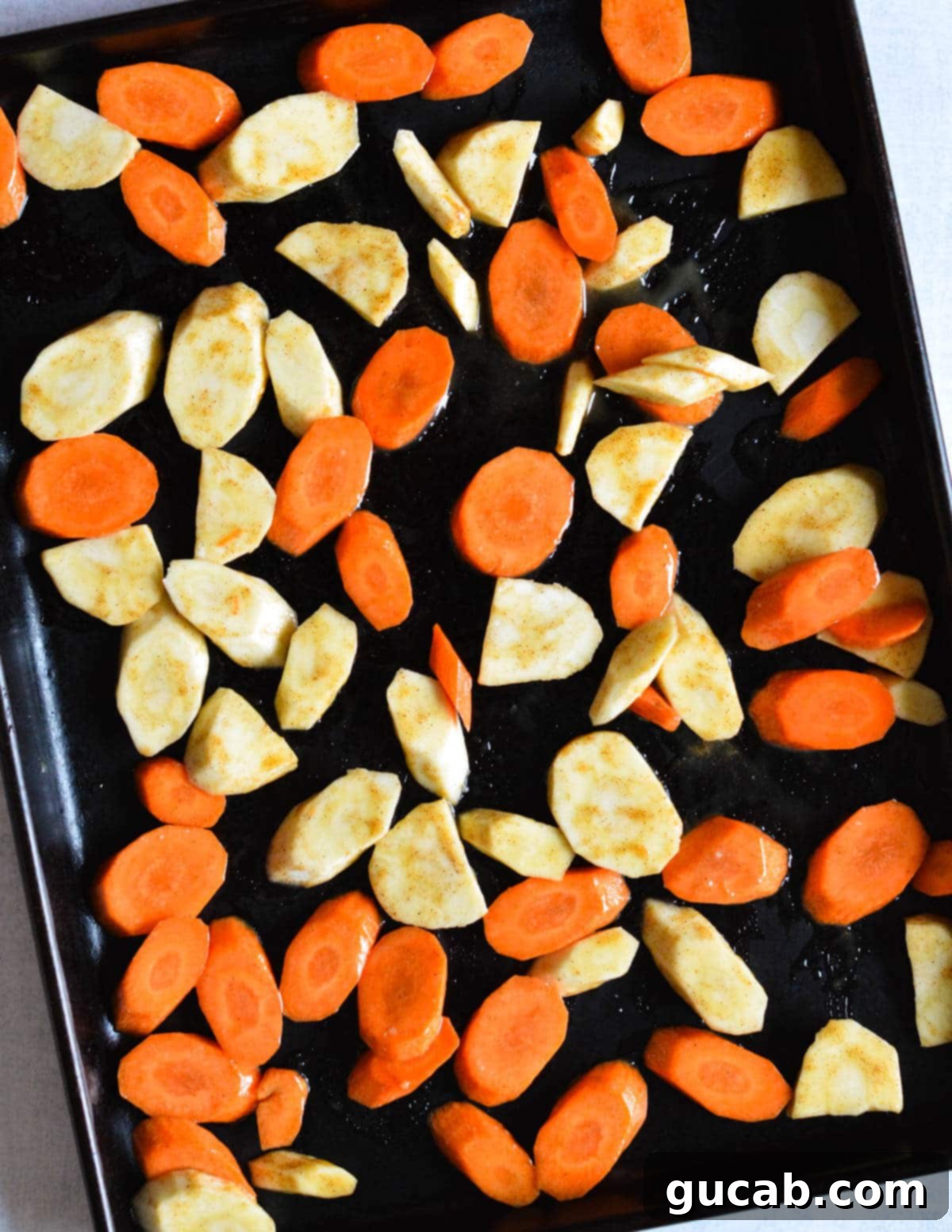 Sliced carrots and parsnips, coated in a honey olive oil mixture, spread out in a single, even layer on a sheet pan, ready for roasting.