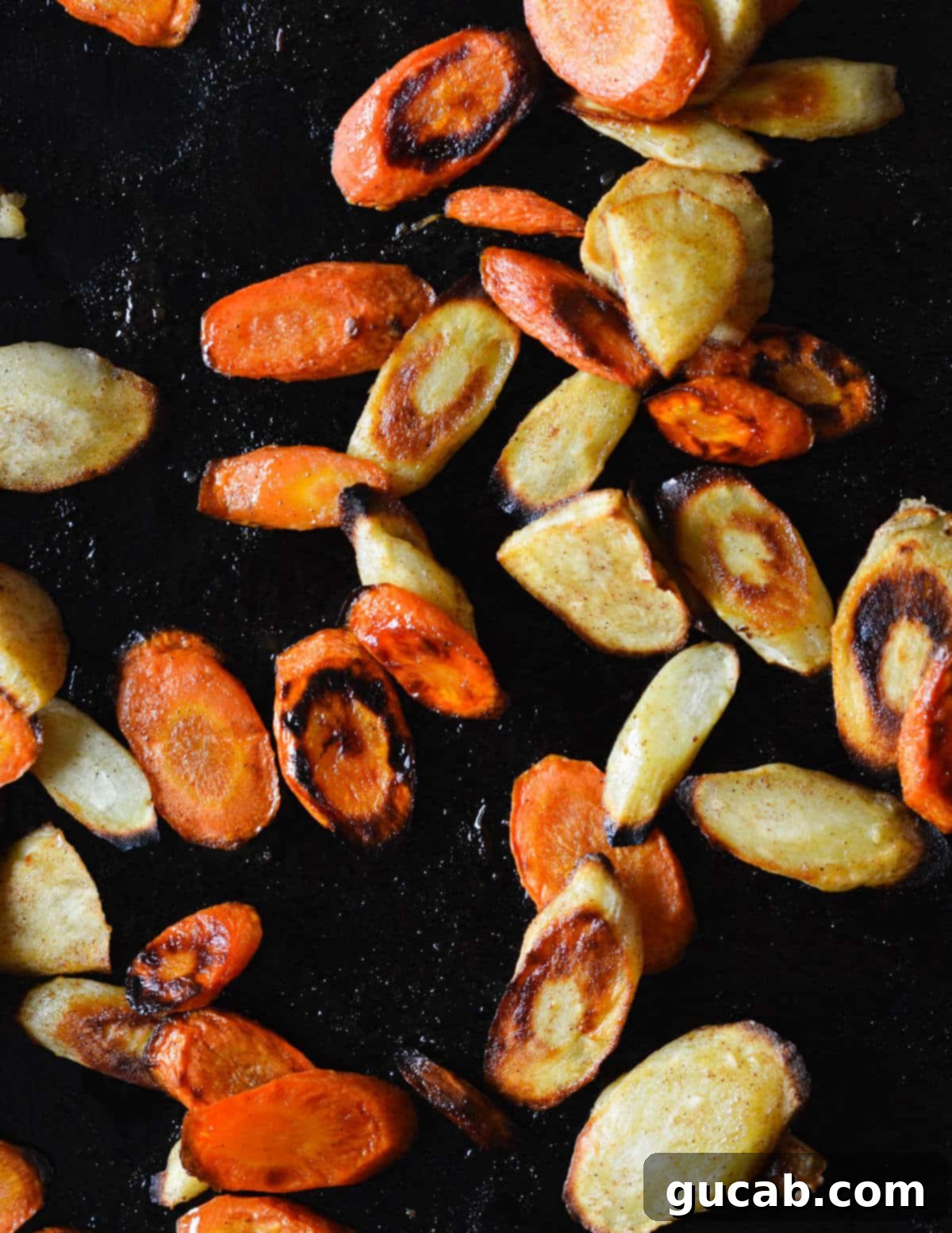 Close up of beautifully caramelized honey roasted carrots and parsnips on a sheet pan, showcasing their golden-brown edges and tender appearance.