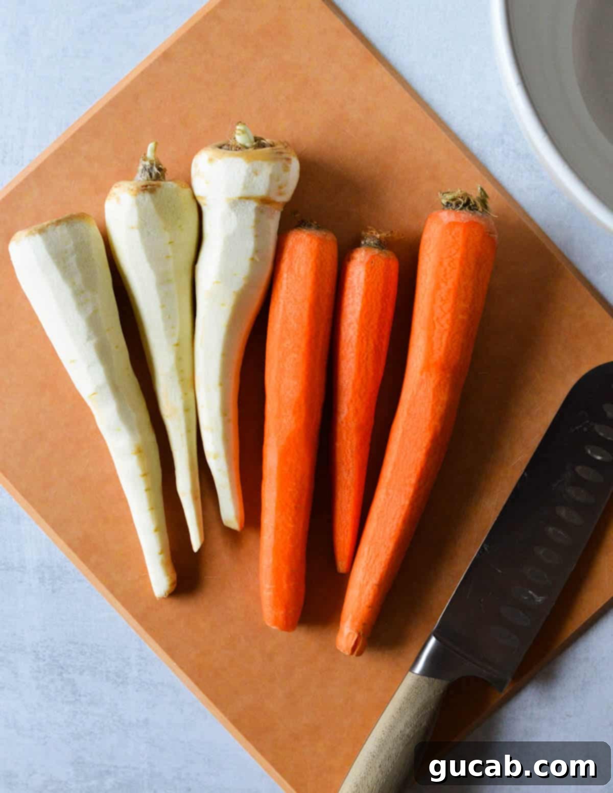 Carrots and parsnips on a cutting board next to a knife, ready for slicing.
