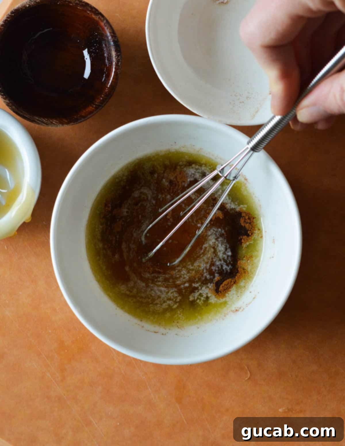 A small bowl with melted butter, cinnamon, honey, and olive oil, with a whisk in the process of combining the ingredients for the glaze.