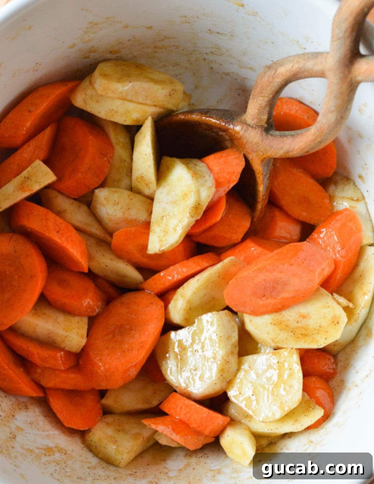 A bowl of sliced carrots and parsnips fully coated in a cinnamon honey and olive oil mixture, glistening and ready for roasting.