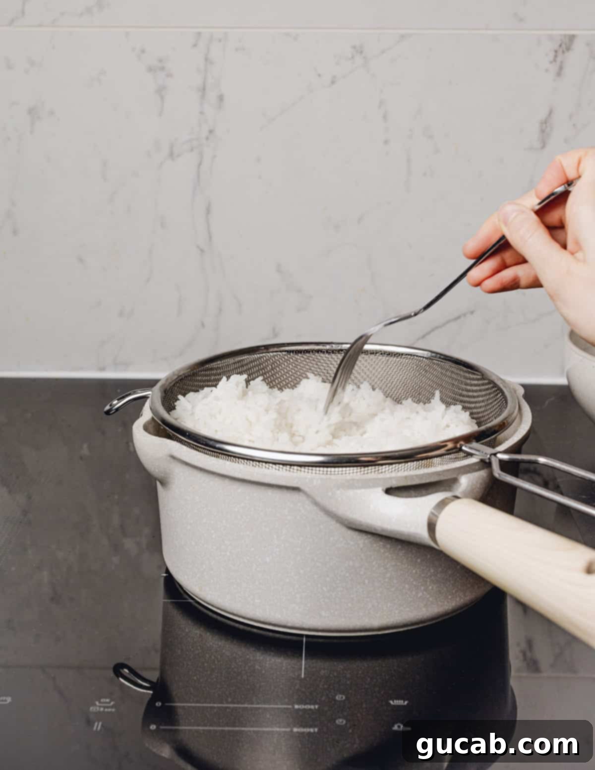 A fork gently fluffing freshly cooked white rice in a strainer.