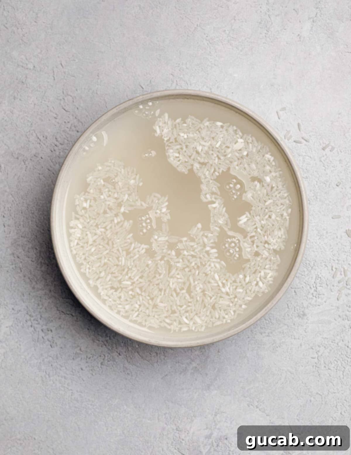 A bowl of white rice soaked in water, showing the cloudy starch being released.