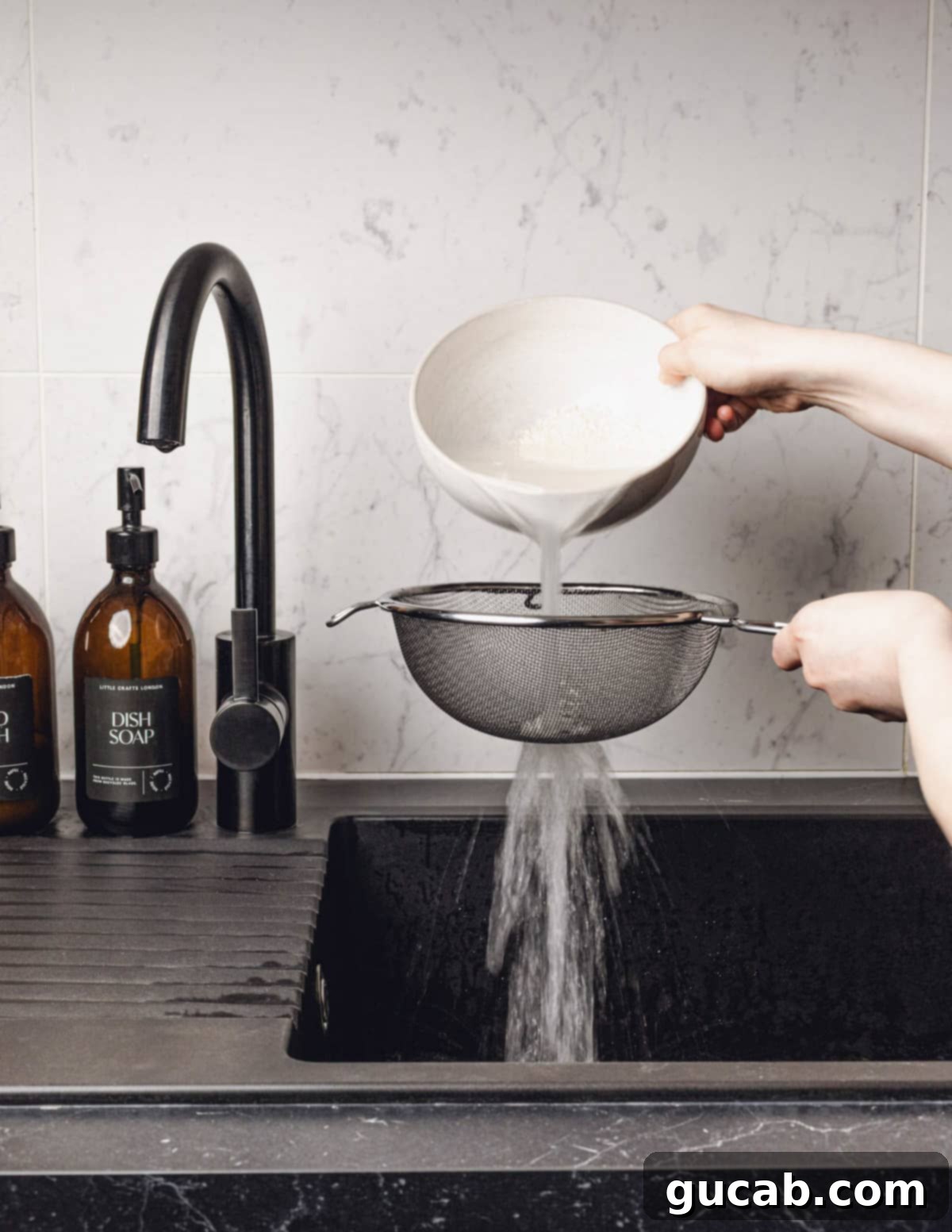 A hand pouring the cloudy soaking water and rice into a handheld strainer to drain.