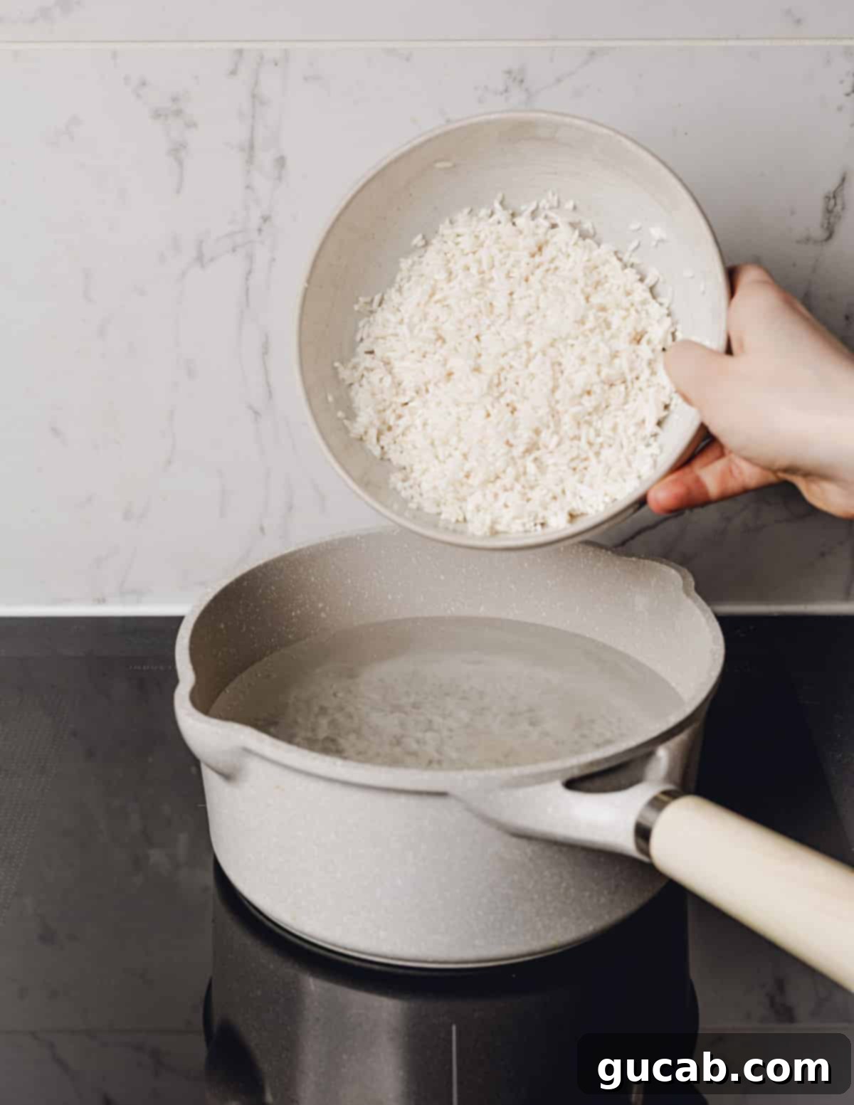 A hand carefully pouring the soaked and drained rice into a pot of vigorously boiling water.