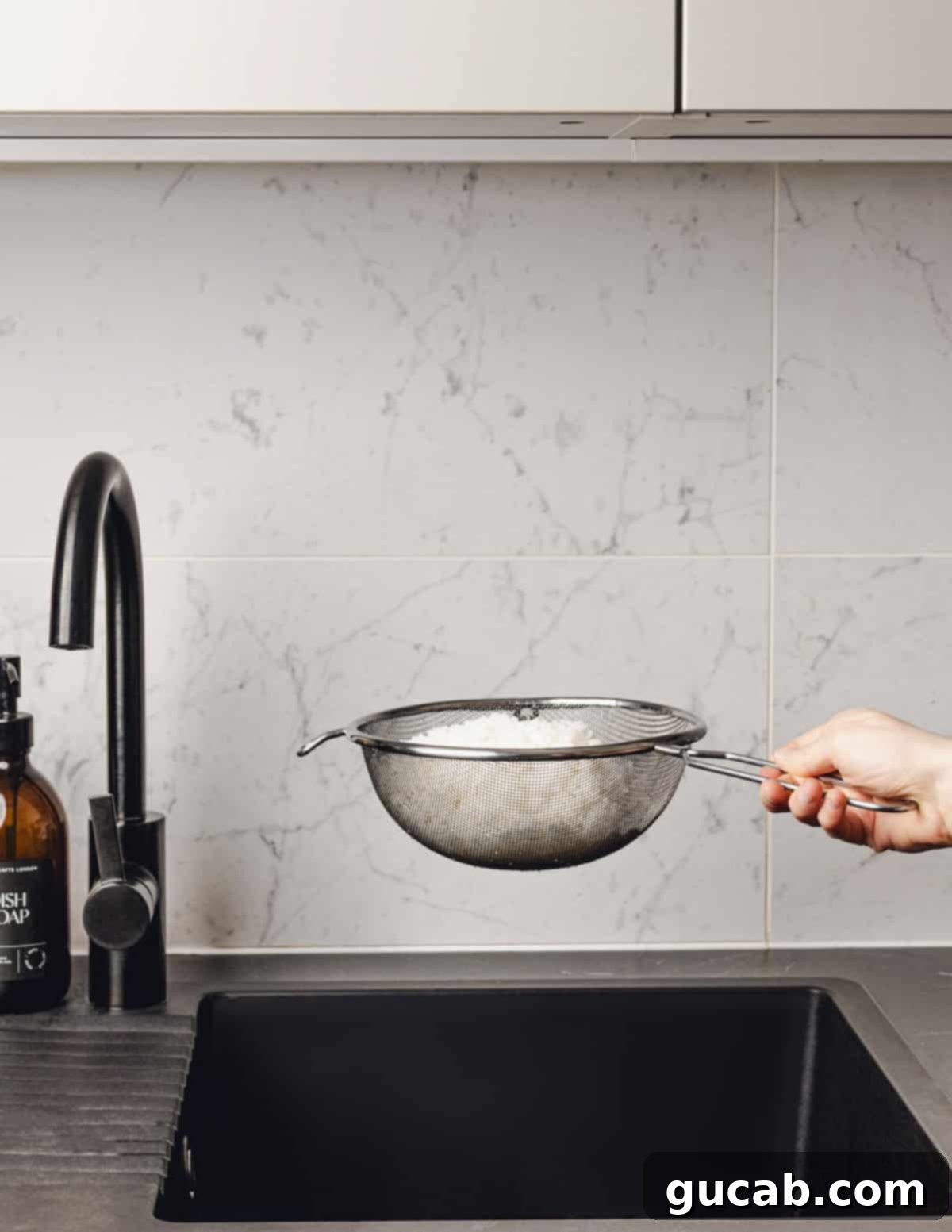 A hand holding a sieve filled with freshly cooked, drained white rice, showing its fluffy texture.