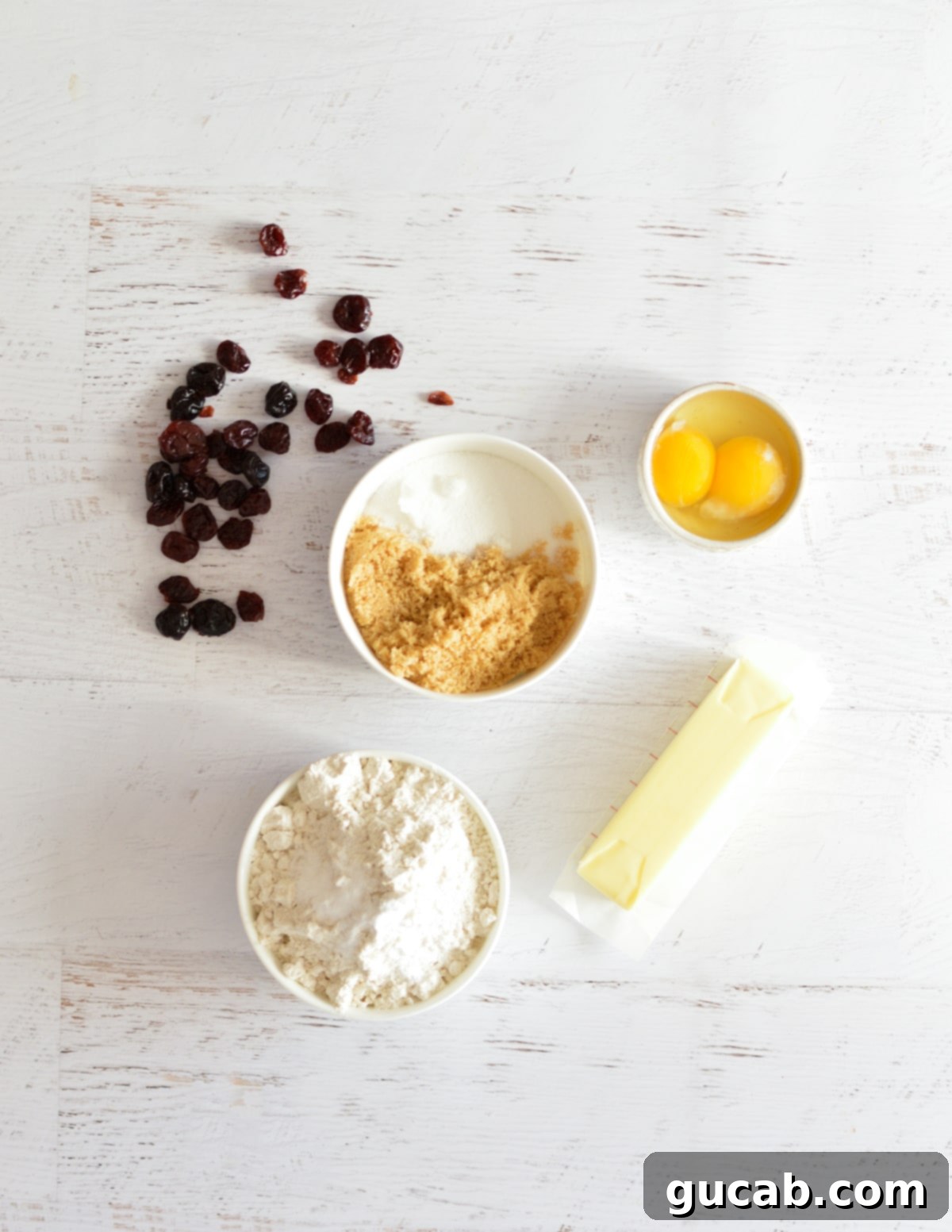 A flat lay of key ingredients for dried cherry cookies, including dried cherries, eggs, flour, butter, and sugar, ready for baking.