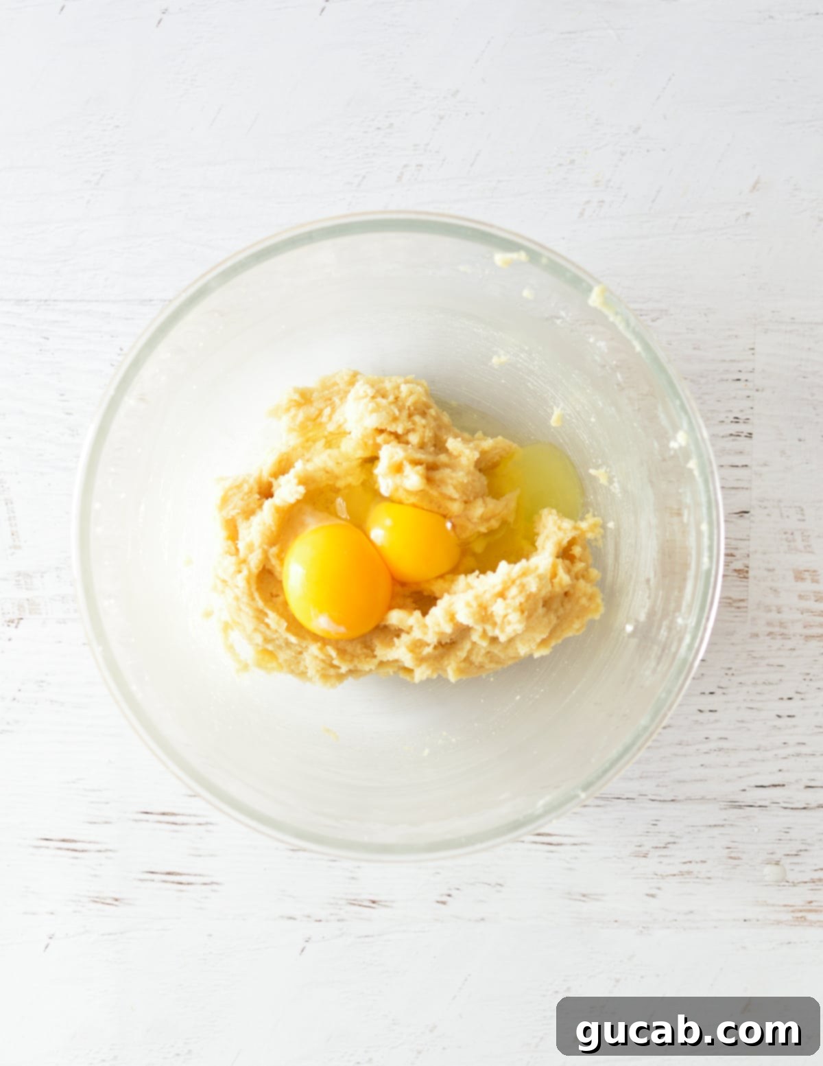 The creamed butter and sugar mixture in a bowl, with a whole egg and an extra yolk placed on top, ready to be mixed.