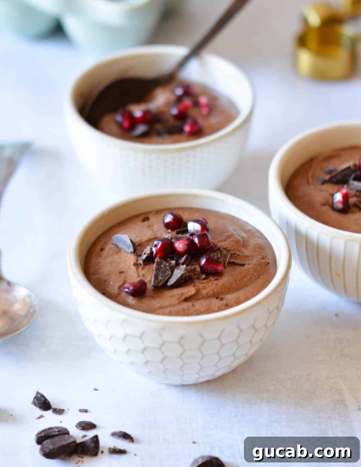 bowls of chocolate mousse with shaved chocolate and pomegranate seeds on top. 