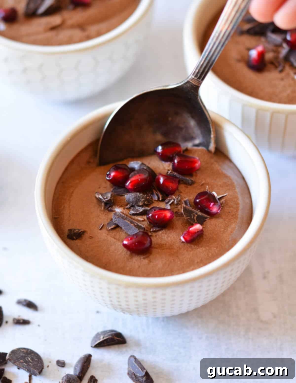 spoon in a cup of chocolate mousse with pomegranate seeds on top. 