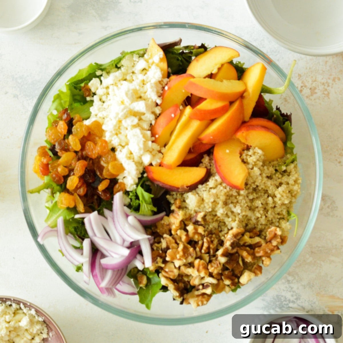 A vibrant quinoa salad featuring feta cheese, fresh peaches, golden raisins (can be swapped for dried cherries), red onions, and mixed greens.