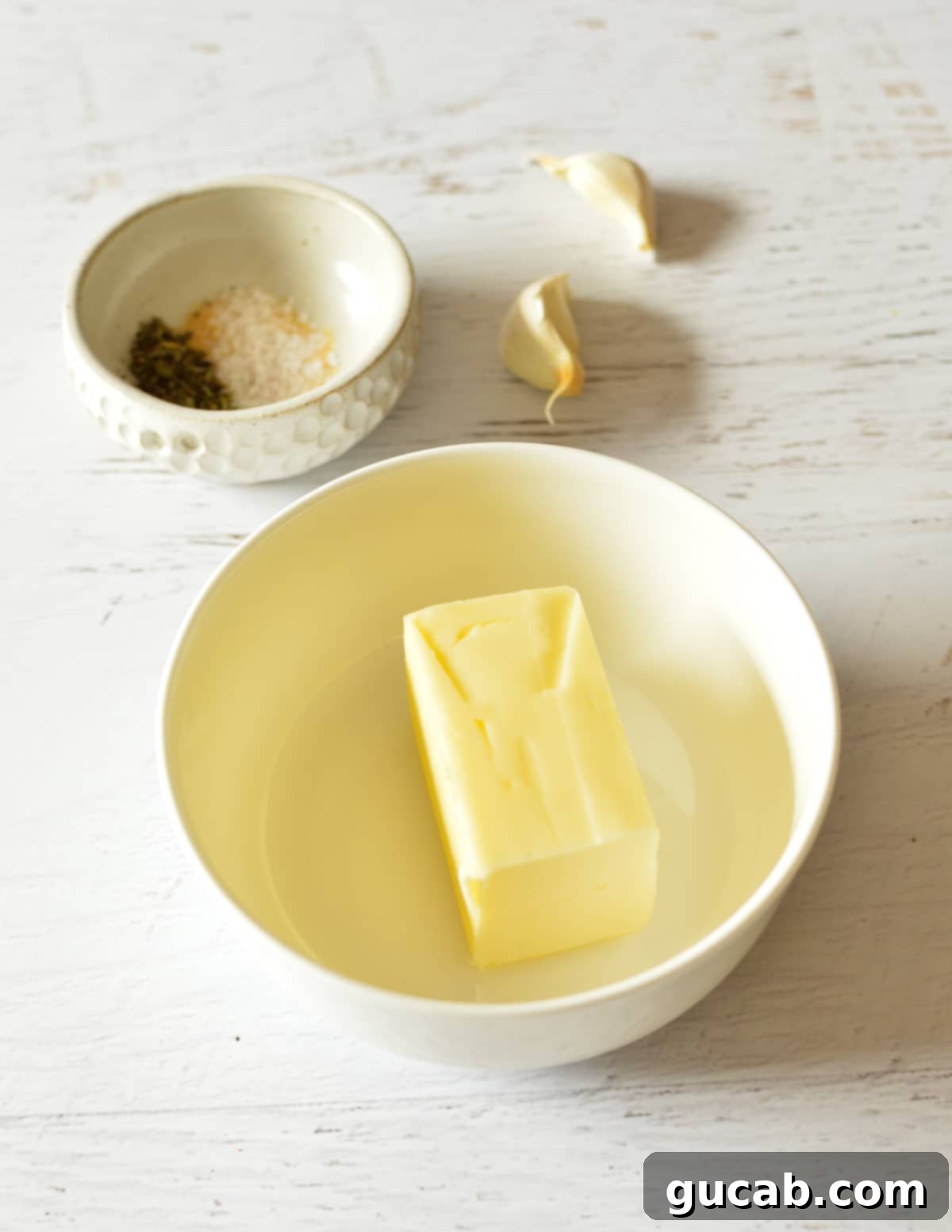 A small bowl filled with softened butter, minced fresh garlic, and a blend of spices.