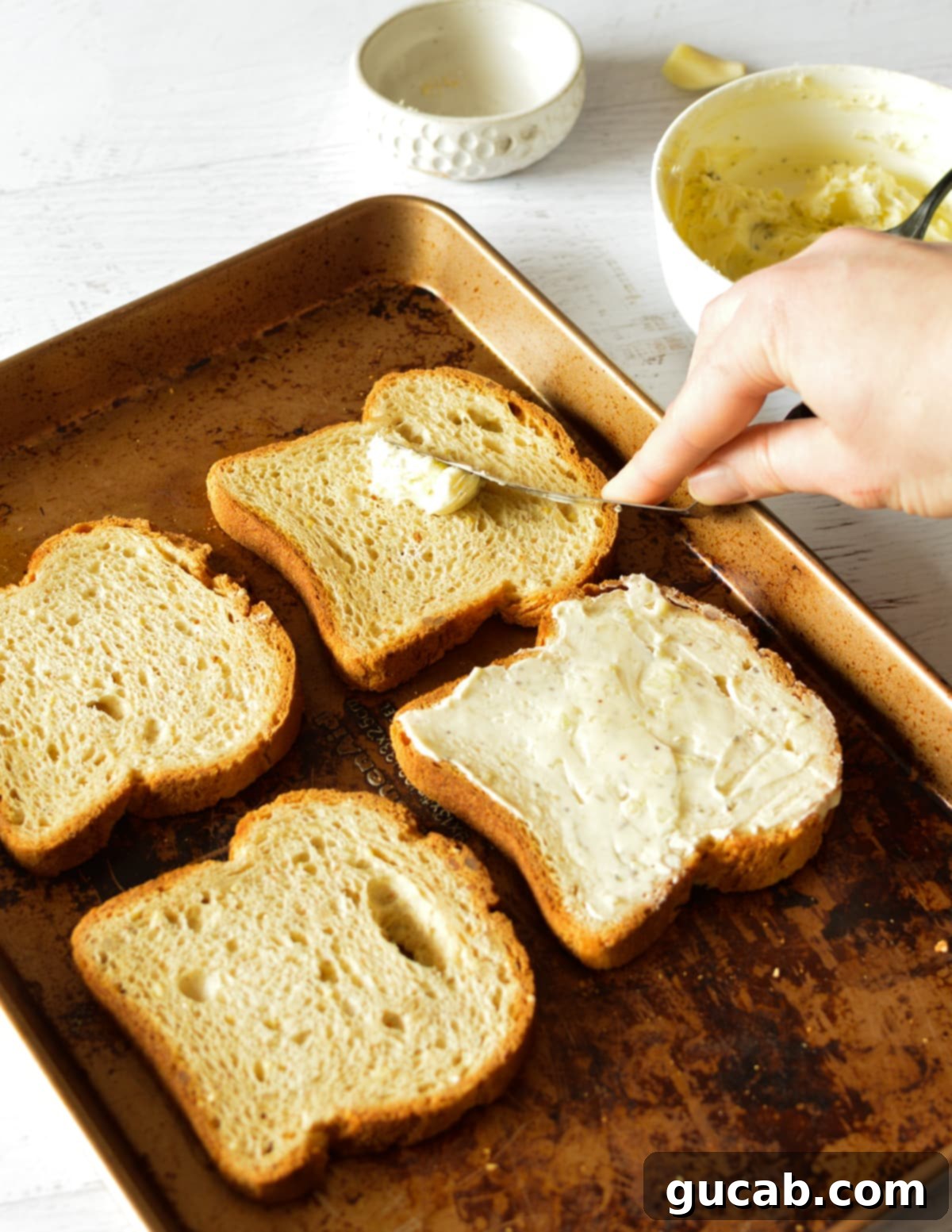 A hand expertly spreading garlic butter onto a slice of bread with an offset spatula.