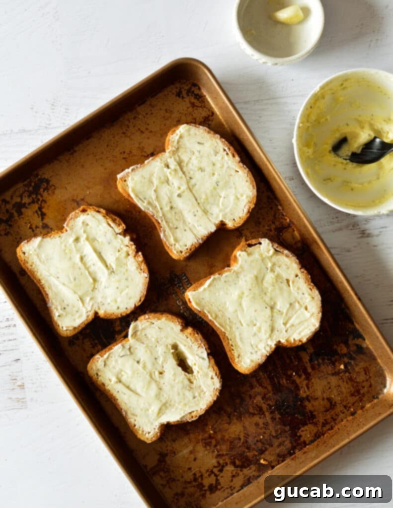 Four slices of bread with melted garlic butter on a baking sheet, pre-broil.