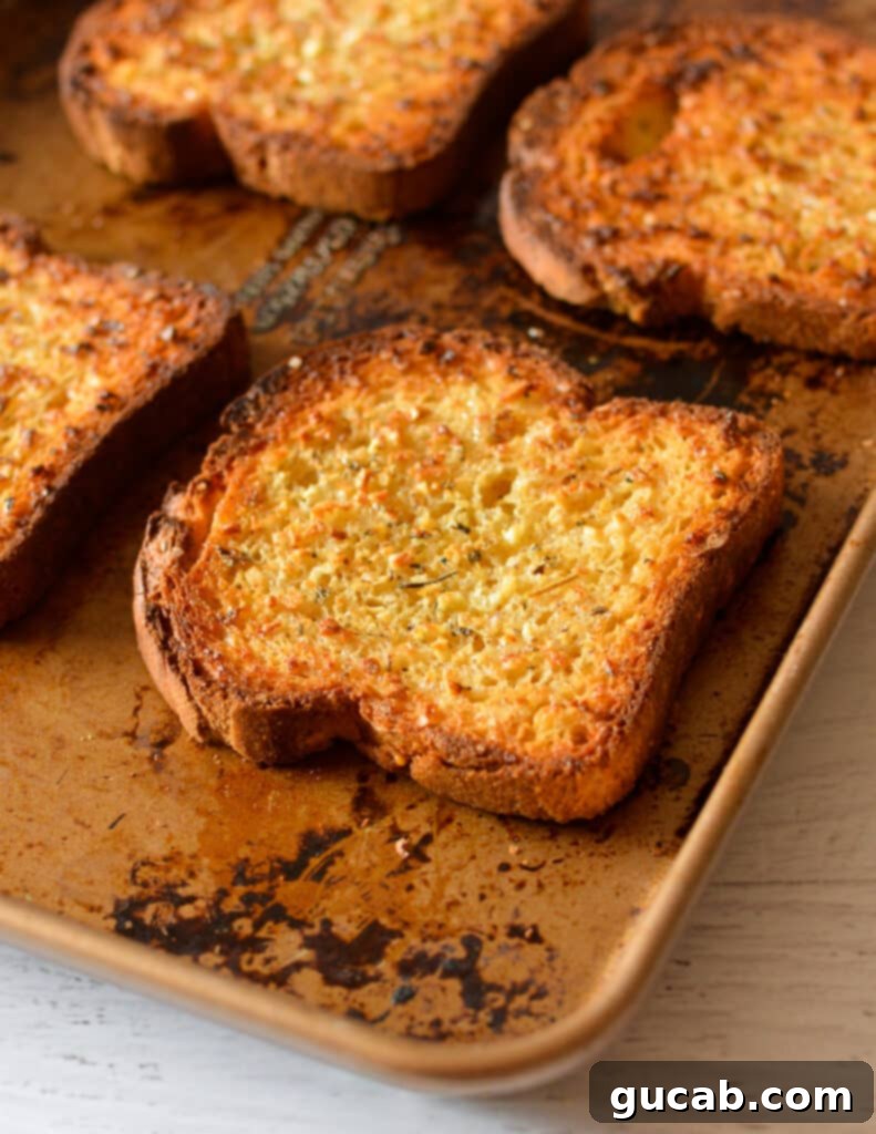 Perfectly golden-brown garlic bread slices on a baking sheet after broiling.