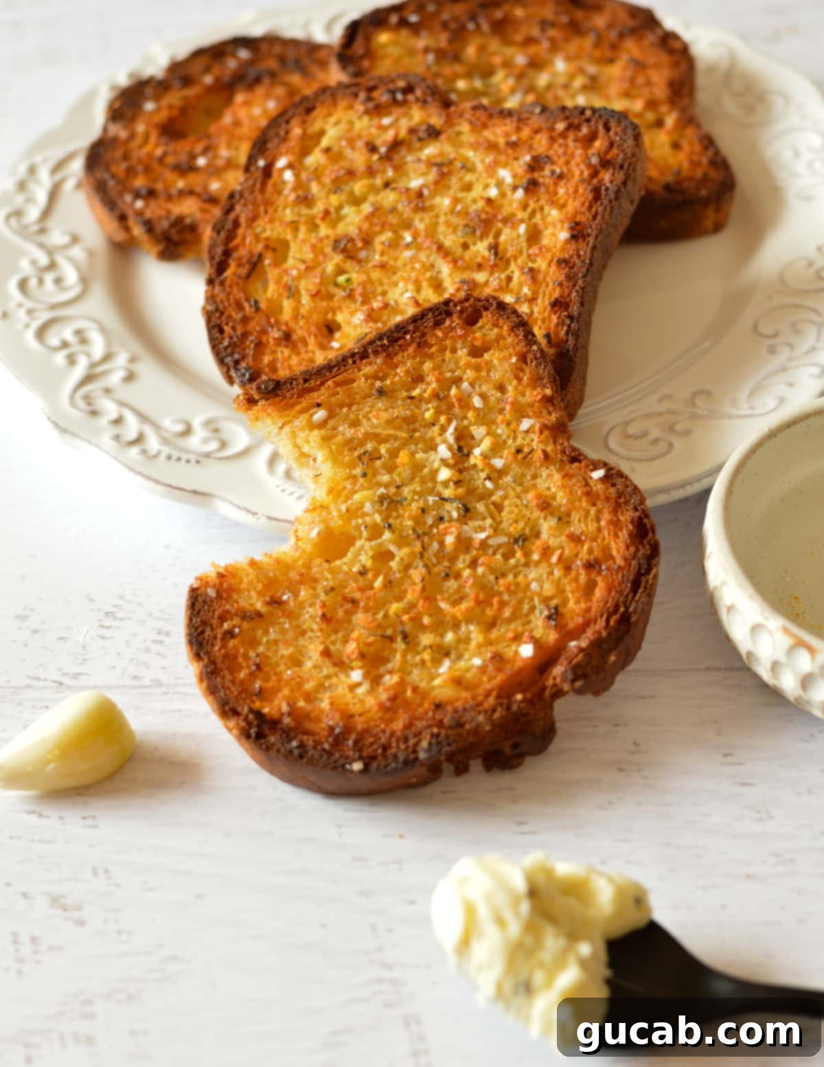 Two pieces of crispy, golden garlic bread on a white plate, ready to be enjoyed.