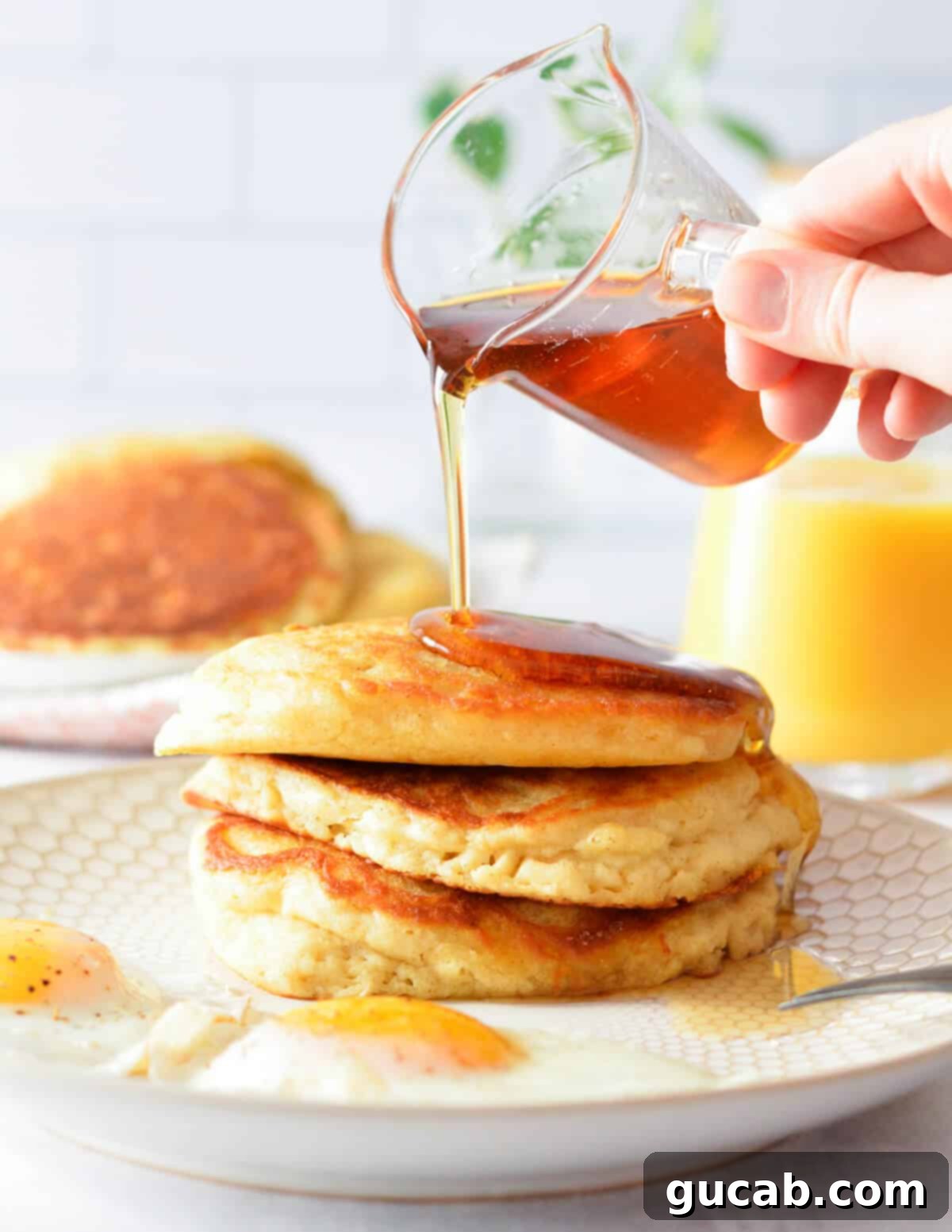 pouring maple syrup onto a stack of fluffy buttermilk pancakes.