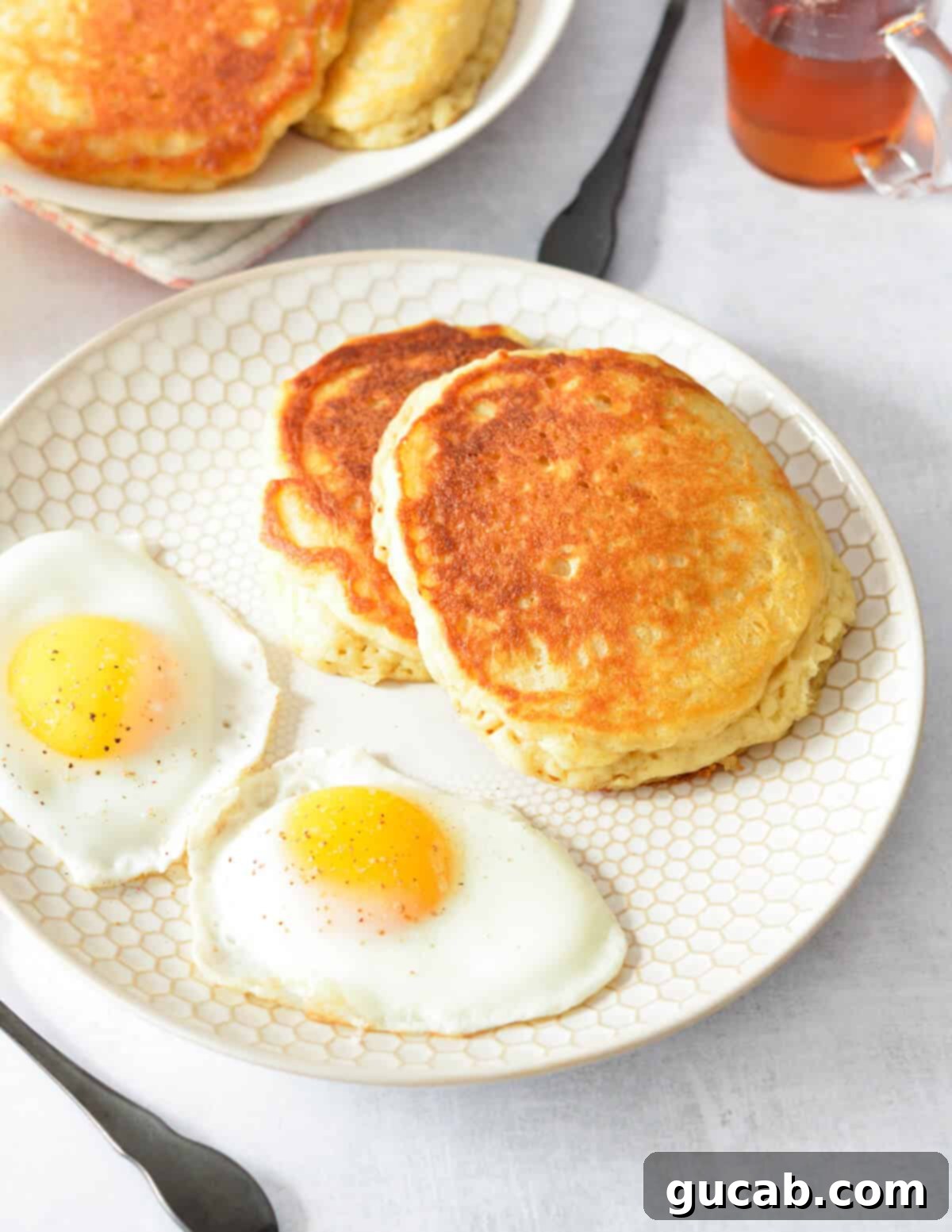 a plate of fluffy buttermilk pancakes served with fried eggs, a complete breakfast.