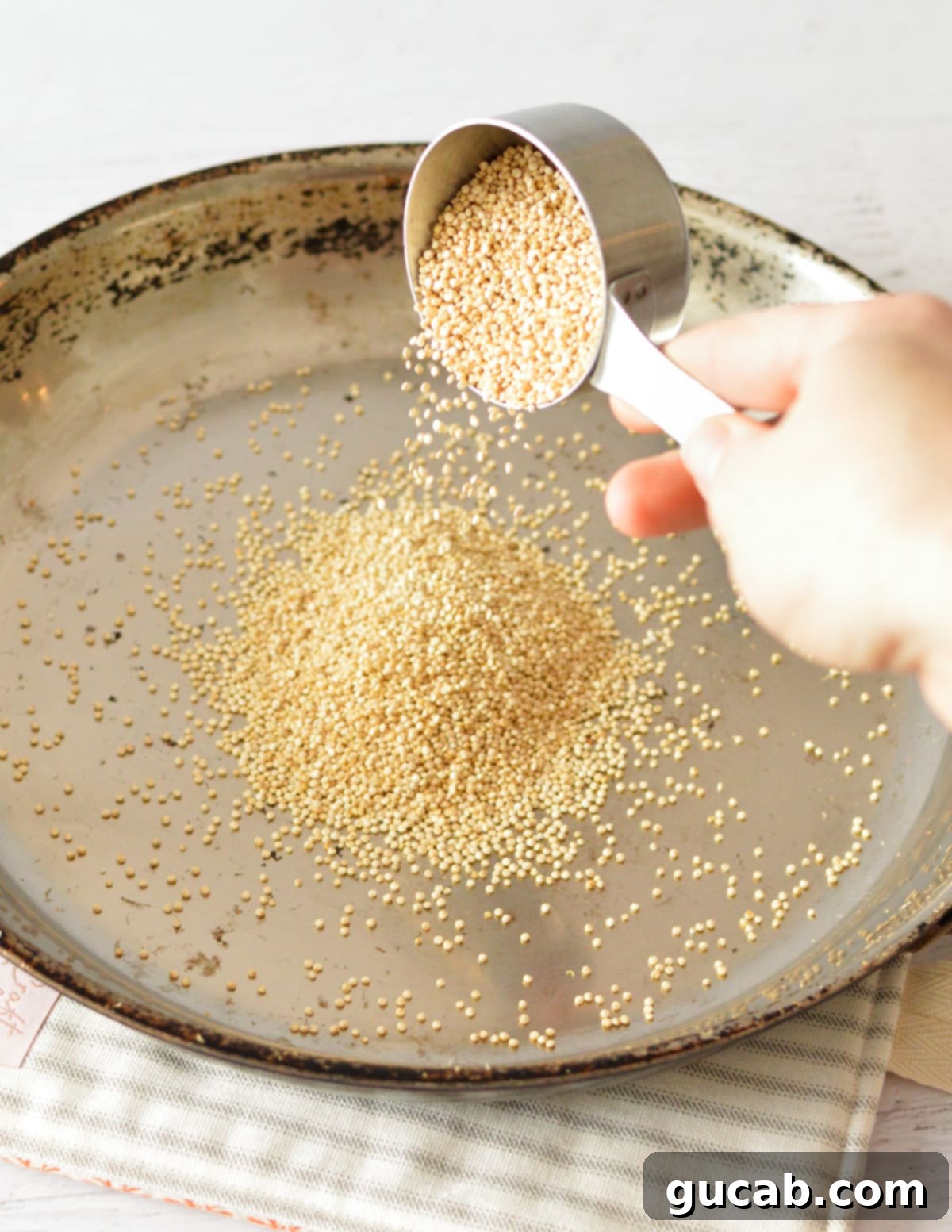 Pouring raw quinoa directly into a hot skillet, ensuring an even spread for popping.