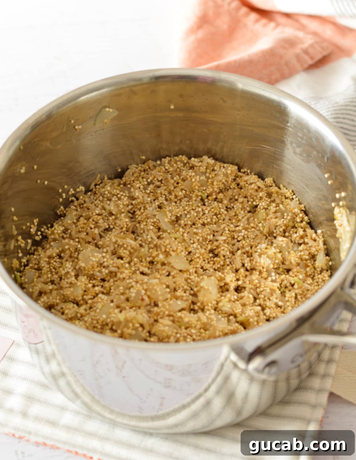 Uncooked brown rice and quinoa added to a saucepan with aromatics, ready for liquid.