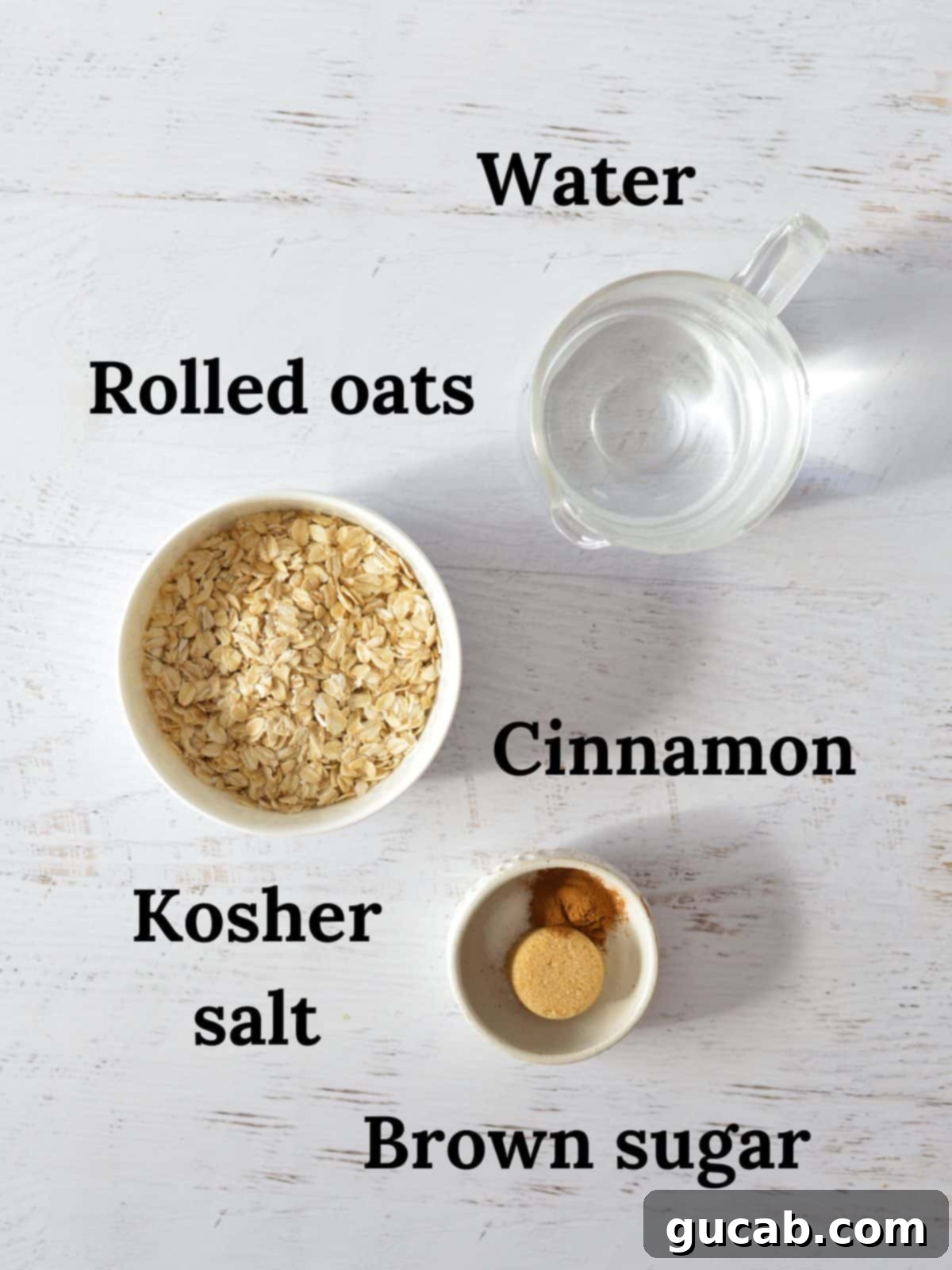 A flat lay of the key ingredients for brown sugar cinnamon oatmeal: a small bowl of rolled oats, a pile of brown sugar, a sprinkle of ground cinnamon, a pinch of kosher salt, and a glass of water.