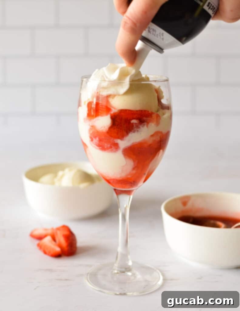 A fully assembled strawberry sundae with sprinkles and a fresh strawberry on top.