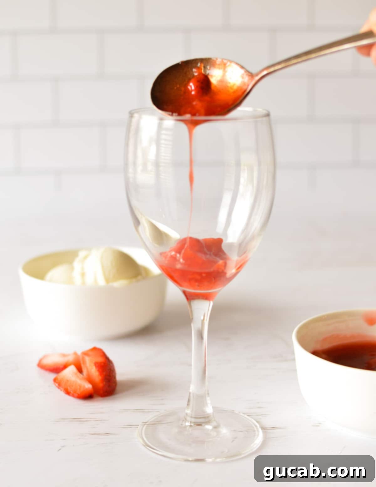 Summer Swirl Indulgence 8 A hand spooning rich, red strawberry sauce into the bottom of a clear glass sundae cup.