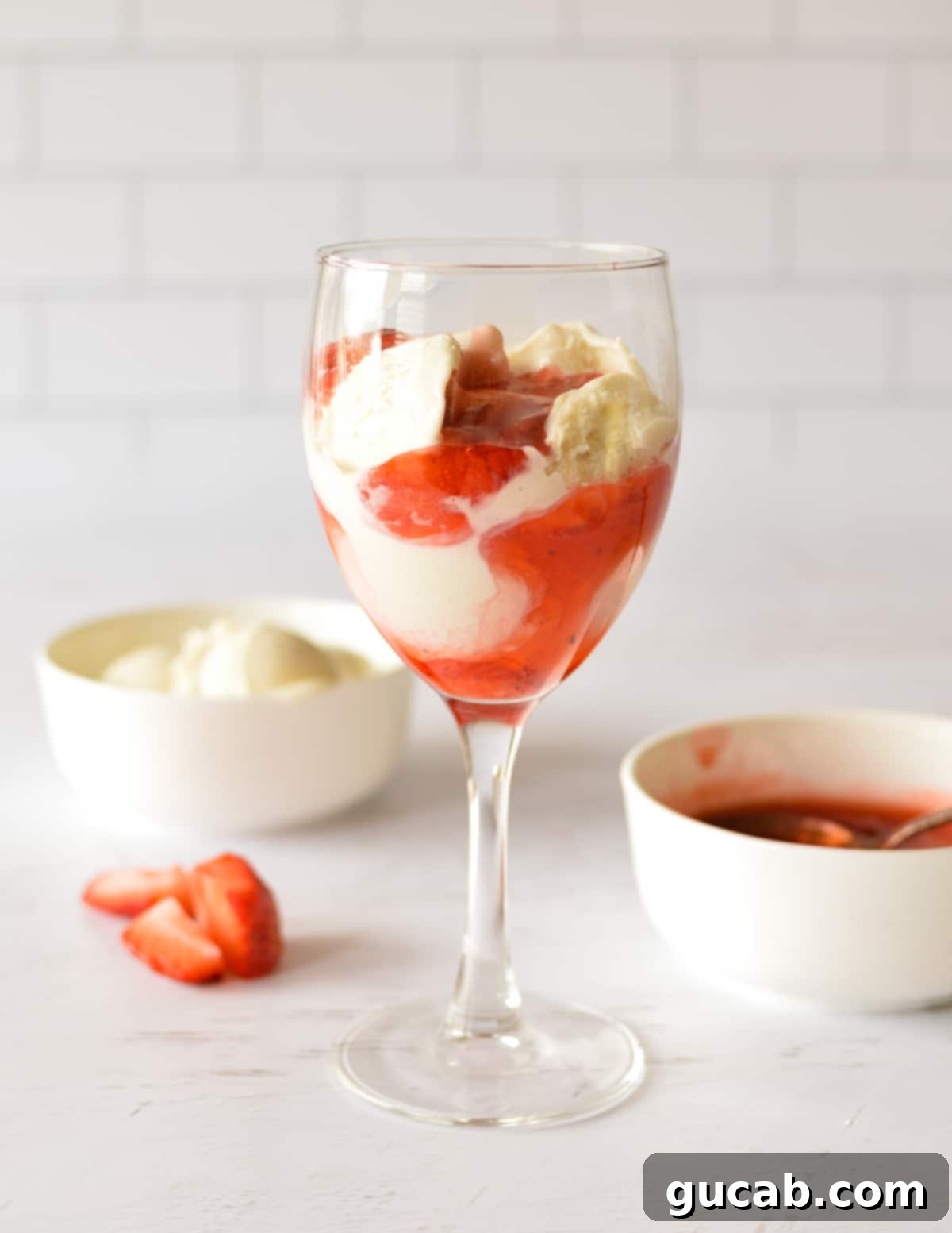 A strawberry sundae in a glass, with layers of sauce and ice cream.