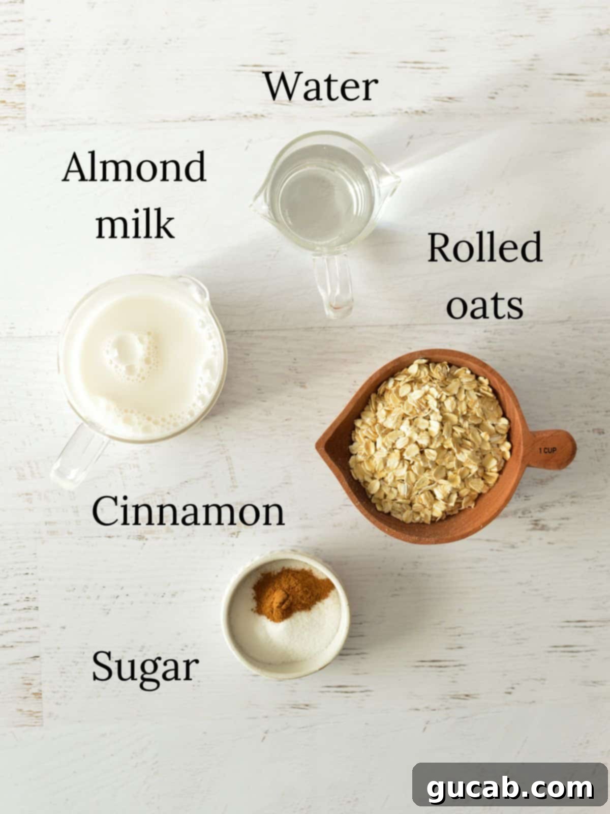 Cozy Cinnamon Oatmeal 3 Essential ingredients for homemade cinnamon oatmeal: Water, rolled oats, almond milk, ground cinnamon, and granulated sugar laid out on a surface.