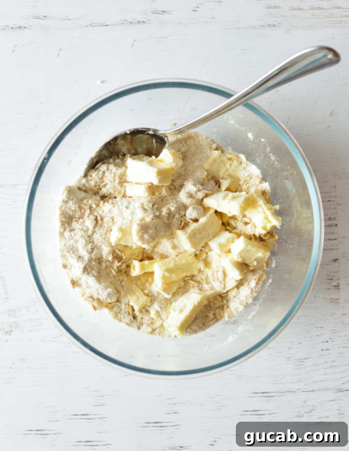 Cold butter cubes being added to the flour, sugar, and oat mixture in a bowl.