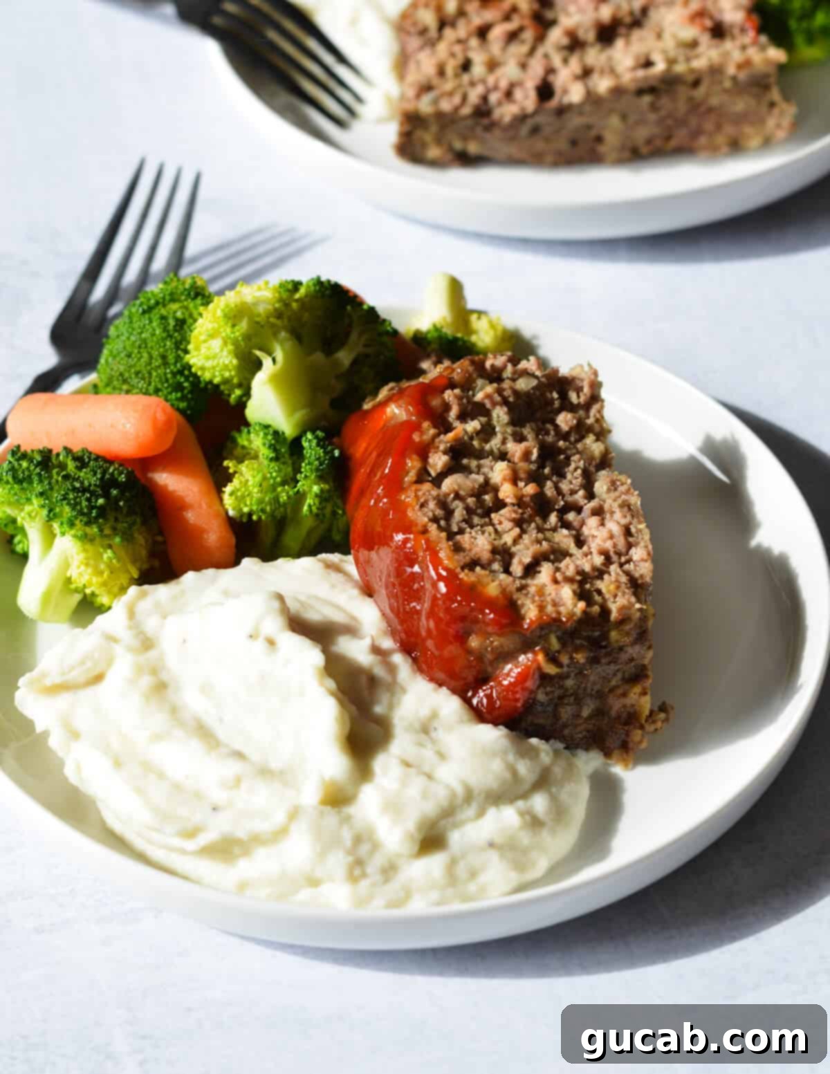 a slice of meatloaf on mashed potatoes with broccoli. 