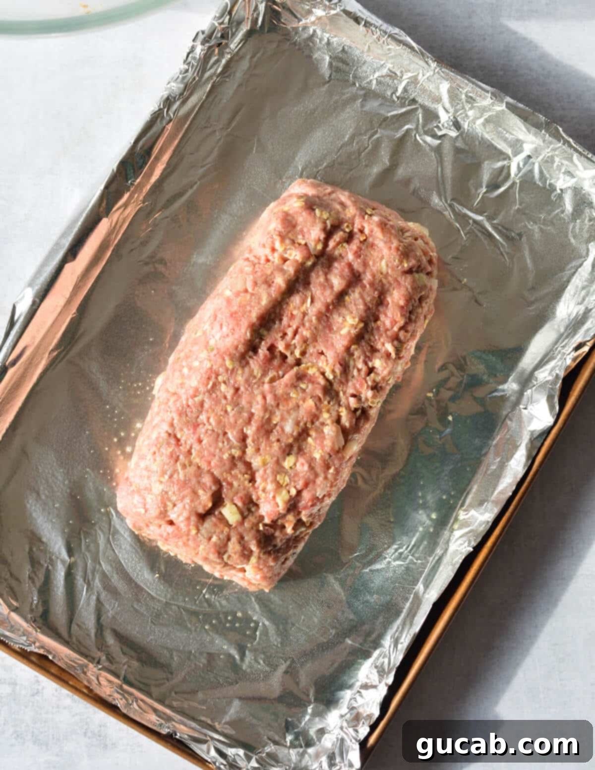 raw meatloaf on a sheet pan lined with aluminum foil. 