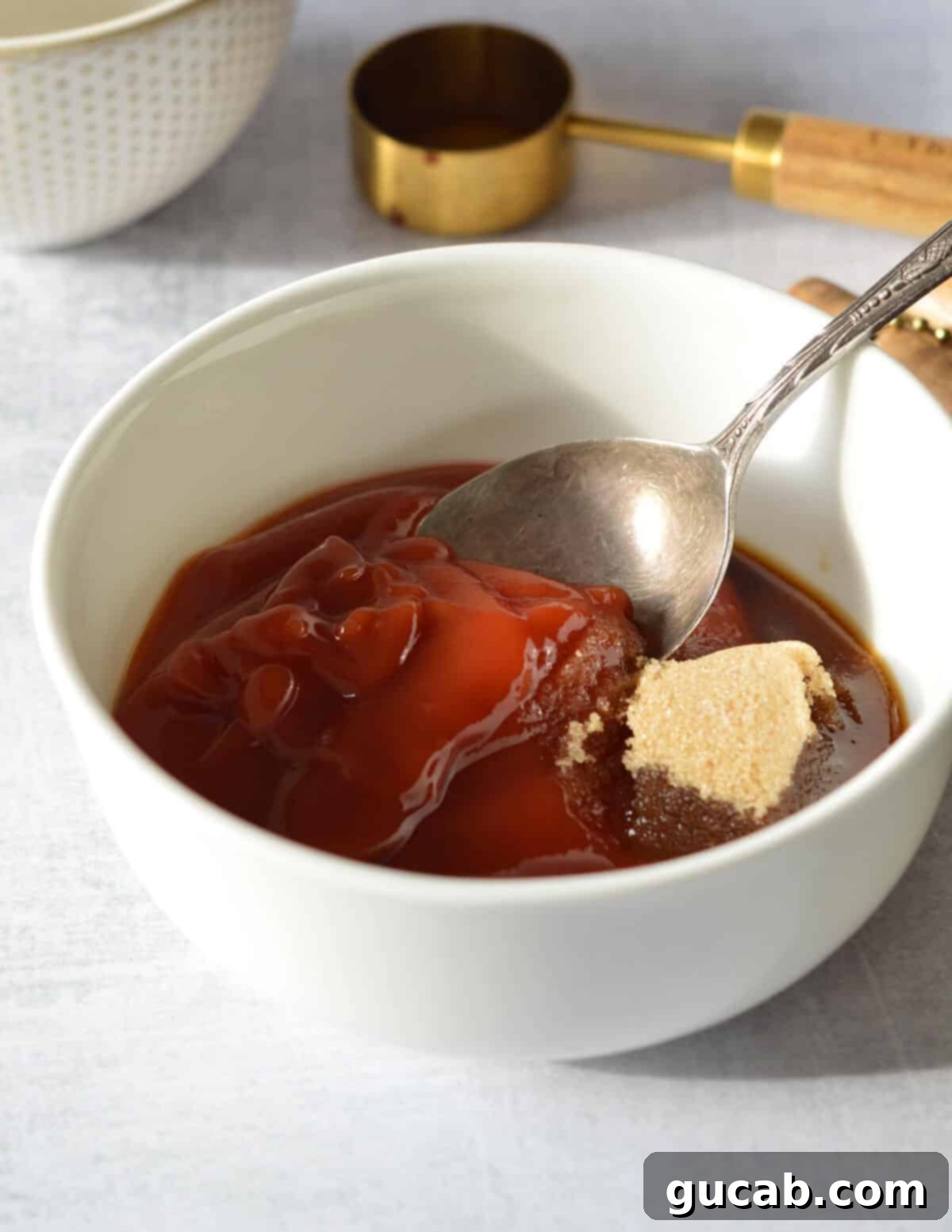 a bowl with ketchup, brown sugar, and a spoon in it.