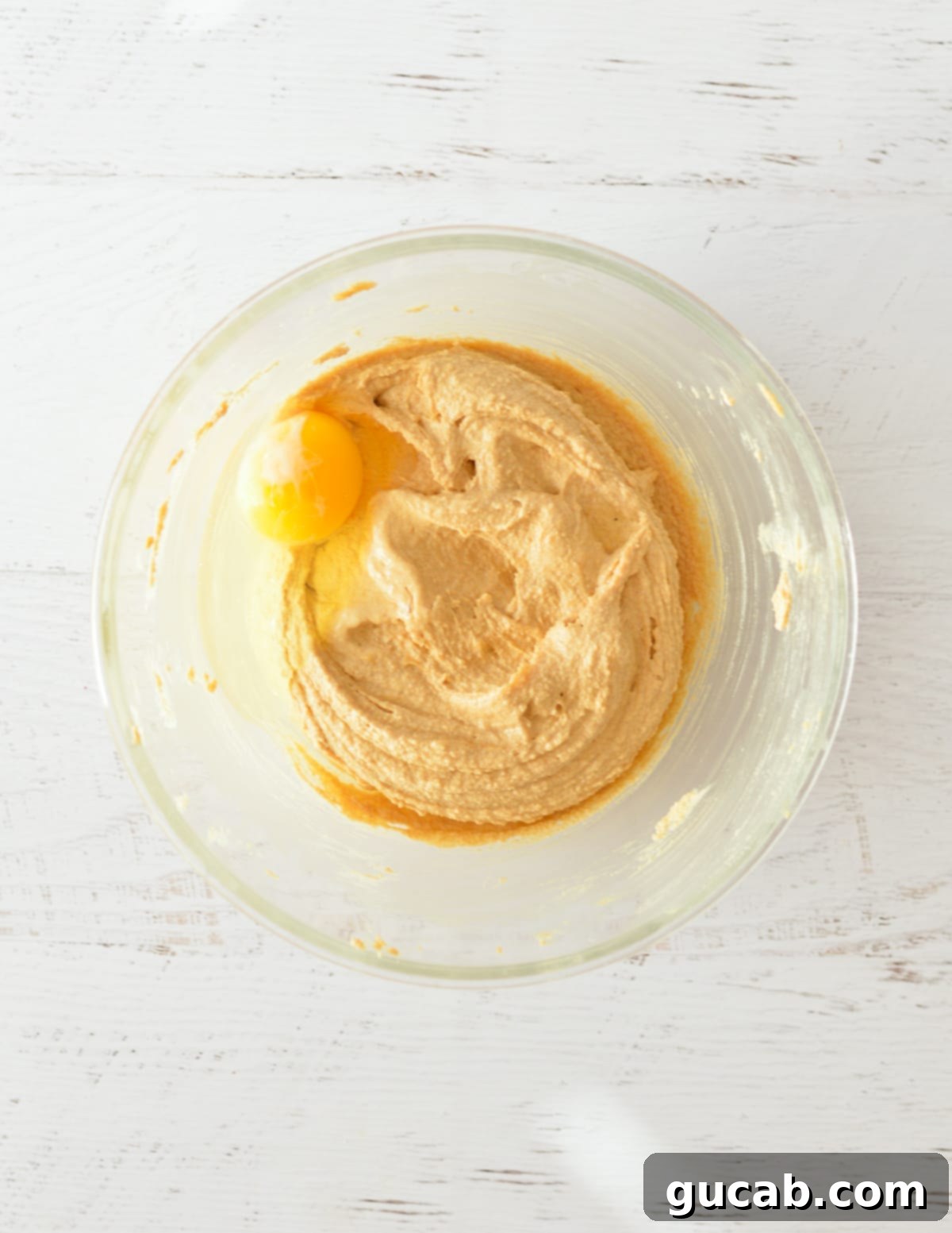 Creamed butter and peanut butter mixture with a single egg on top, ready to be beaten.