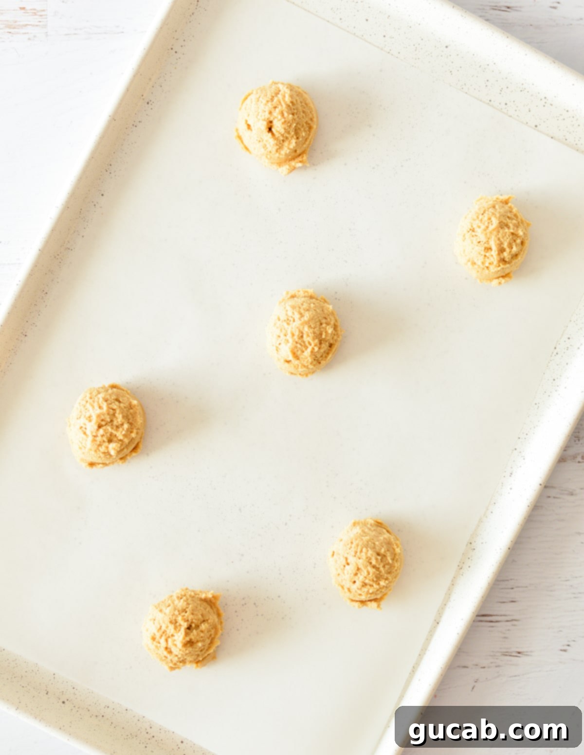 Uniform balls of peanut butter cookie dough scooped onto a parchment-lined sheet pan, spaced for baking.