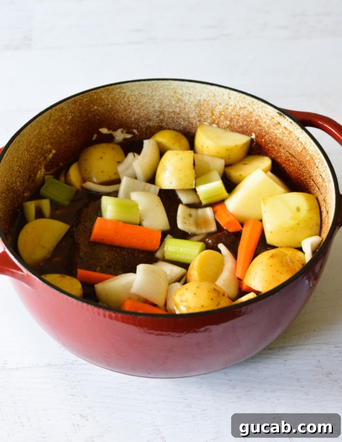 chuck roast in a pot with potatoes, carrots, and onions. 