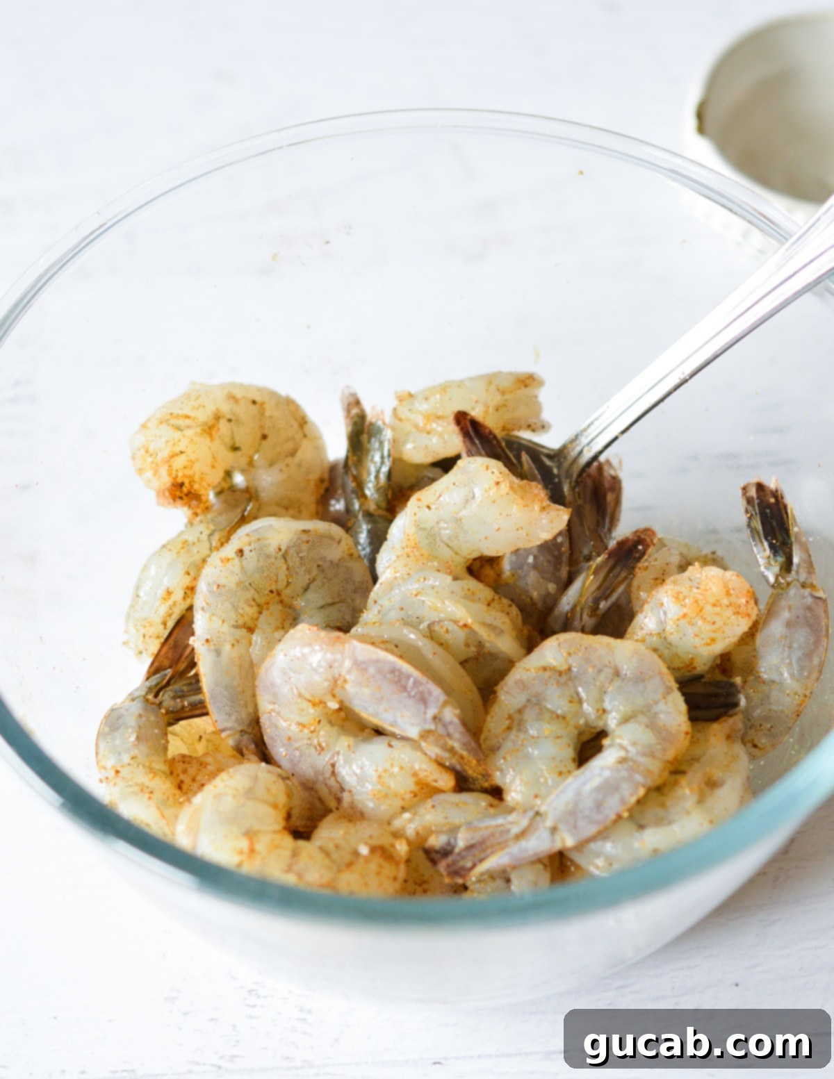 A bowl of shrimp thoroughly tossed in seasoning, ready for pan searing.
