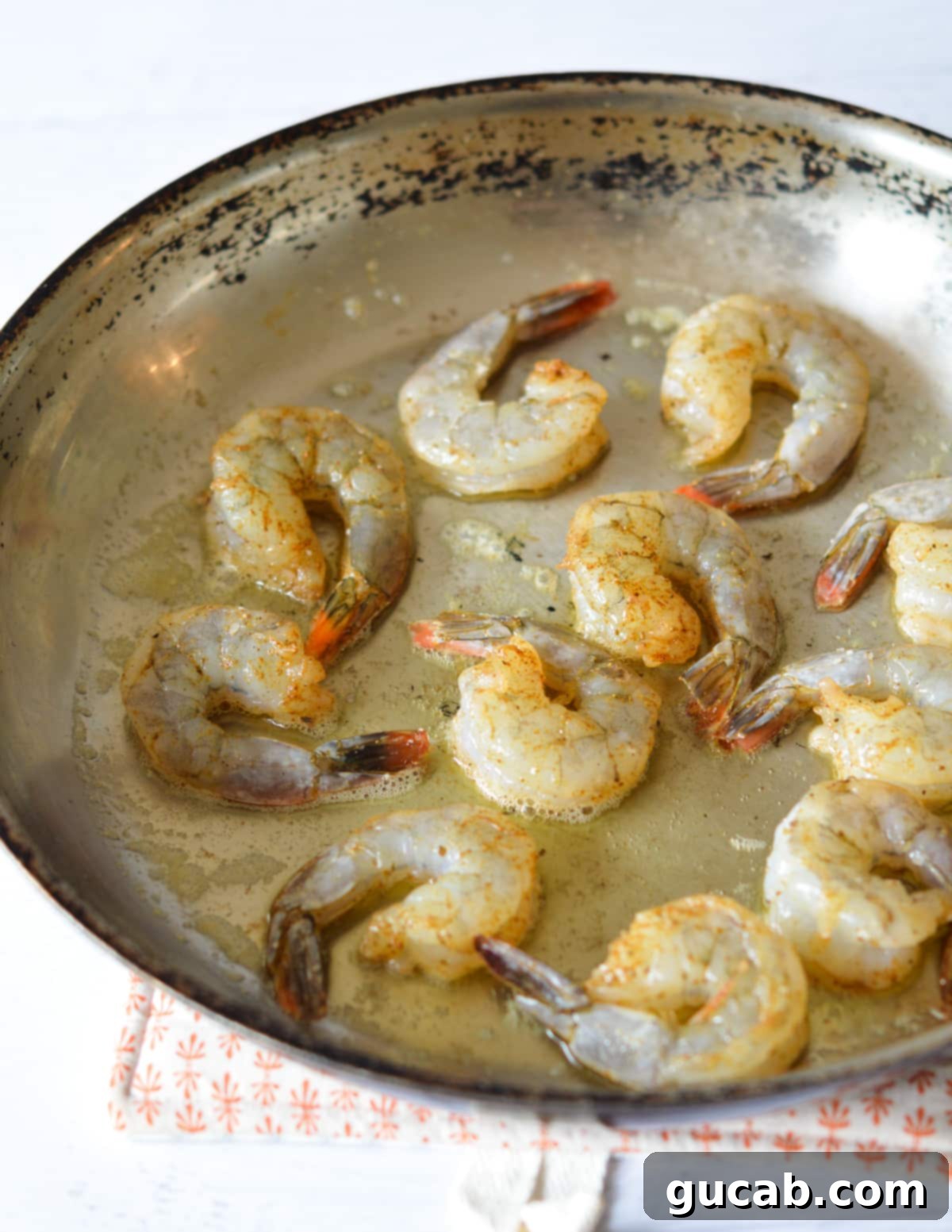 A hot skillet with melted butter and olive oil, with half of the seasoned shrimp added in a single layer.