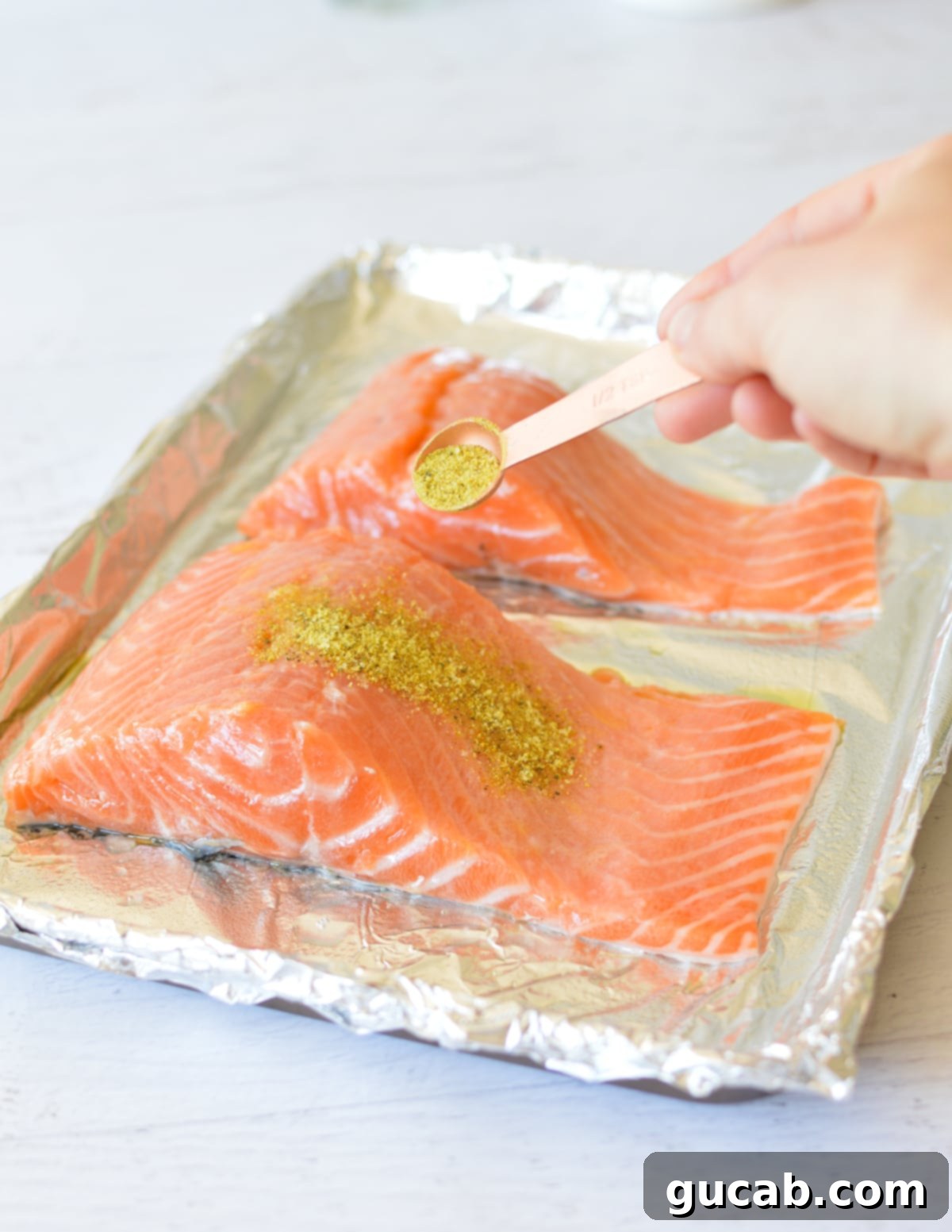 hand sprinkling lemon pepper seasoning on salmon fillets. 
