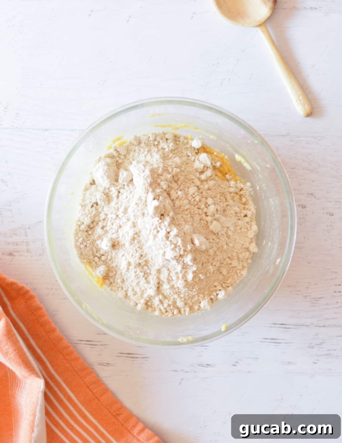 Cookie dough in a bowl with oat flour, baking soda, and salt sprinkled over the top, before being mixed in.