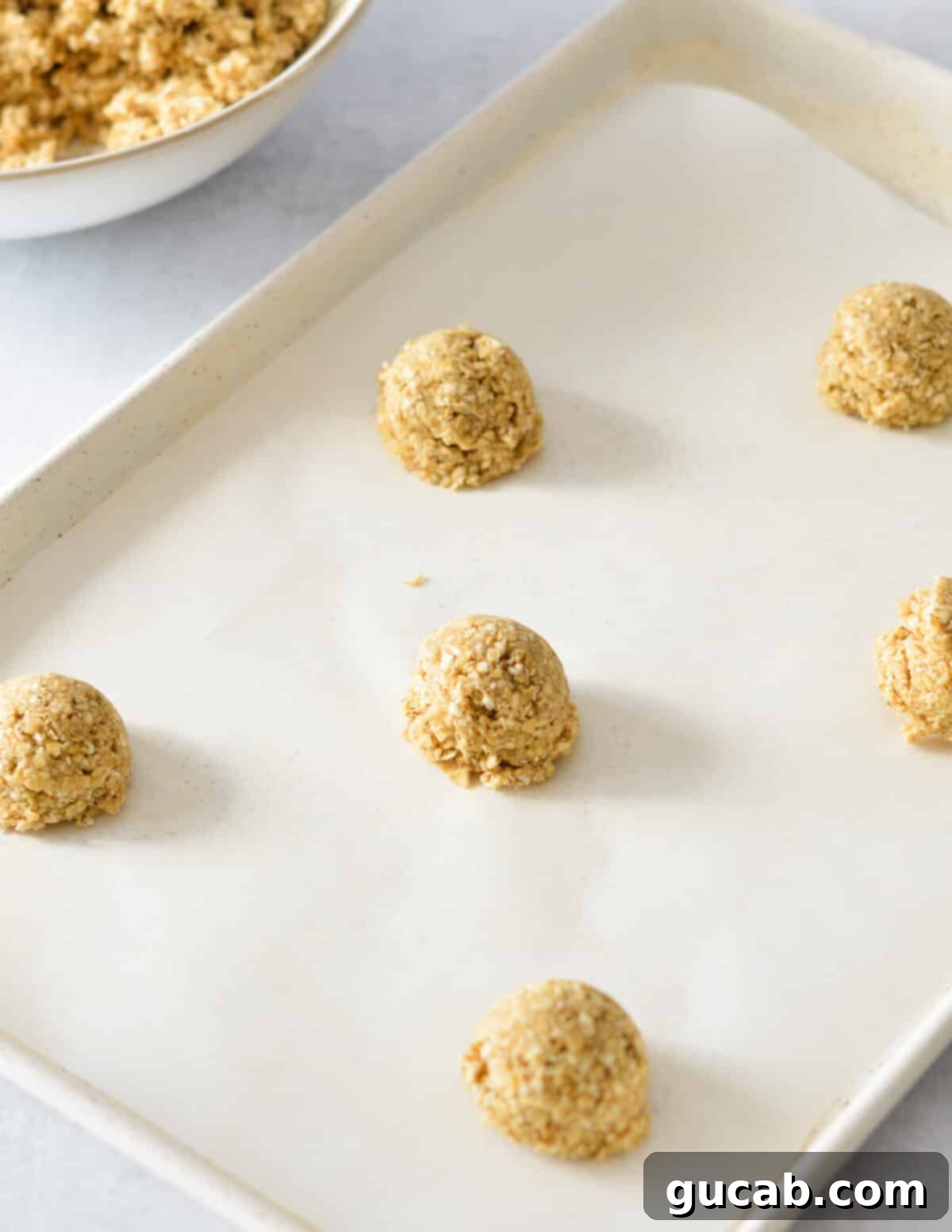 Gluten-Free Oatmeal Cookies 11 Uniform balls of oatmeal cookie dough neatly arranged on a parchment-lined baking sheet, with ample space between them.