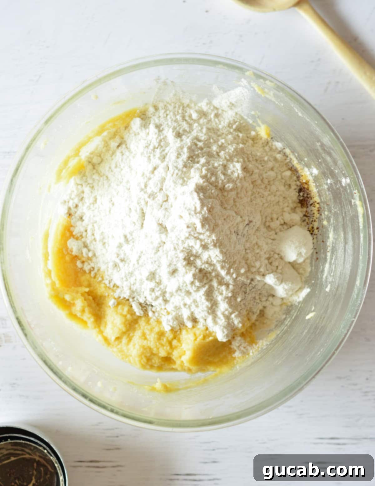 A bowl with the wet cookie mixture, topped with flour and other dry ingredients, ready for mixing.