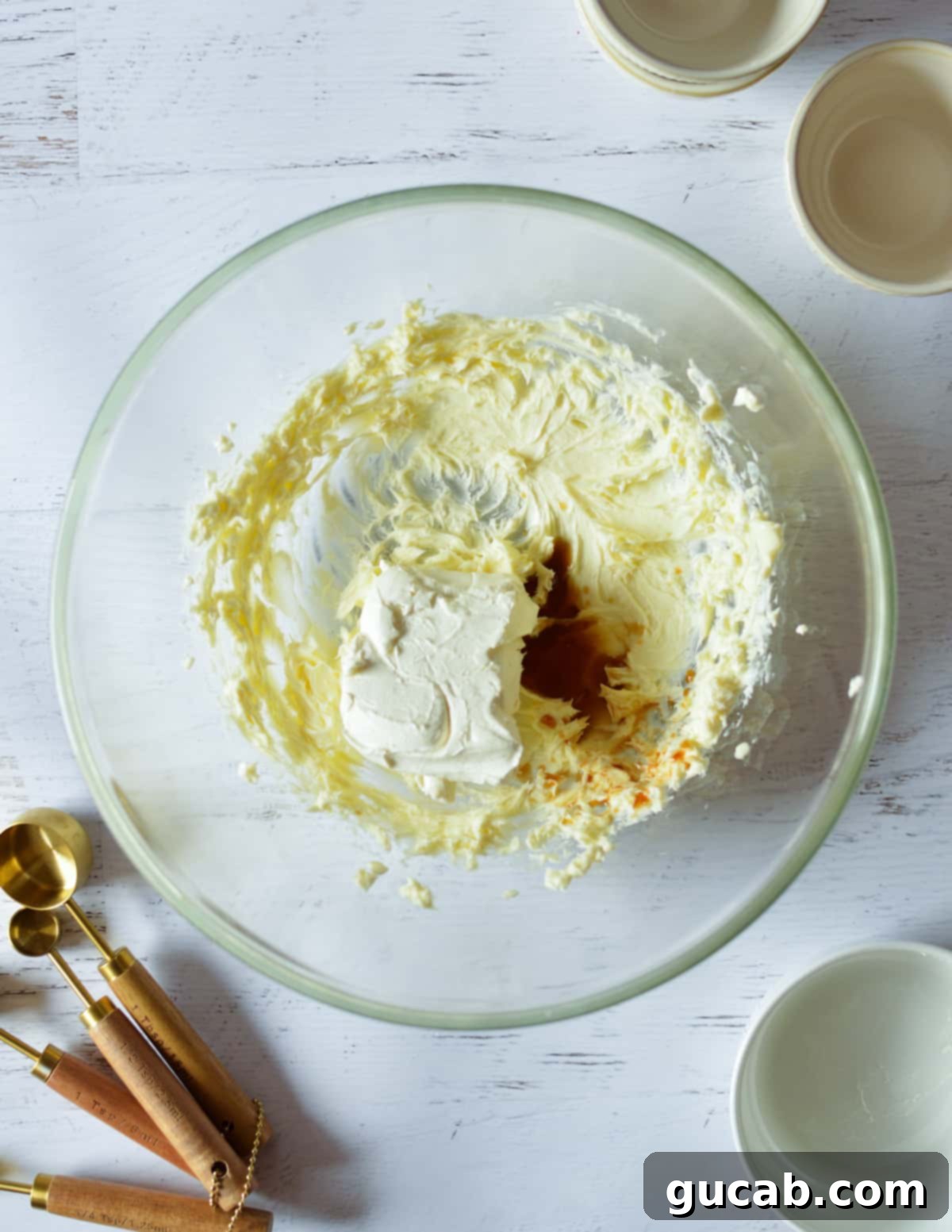 A bowl containing whipped butter, cream cheese, and vanilla extract being mixed.