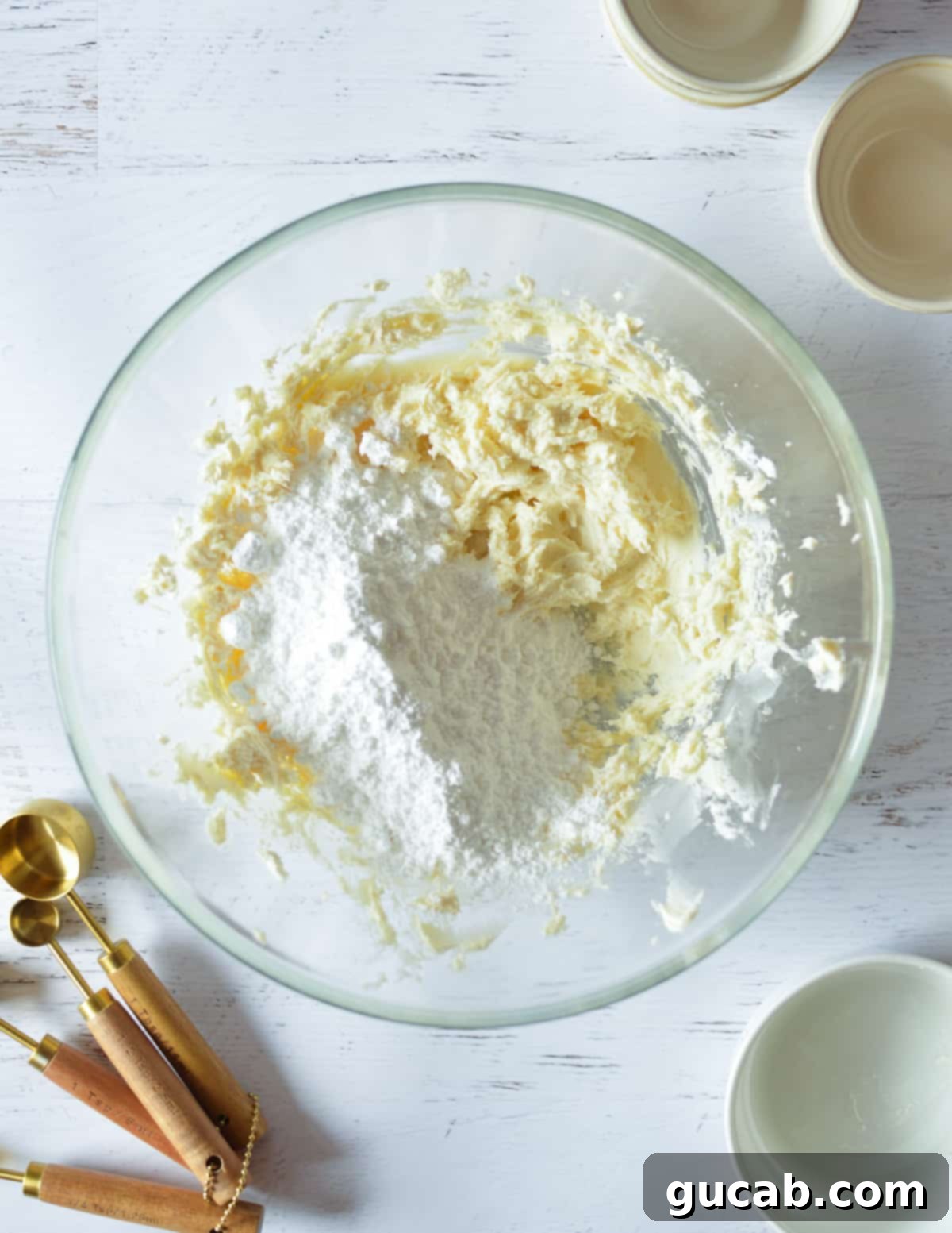 A bowl of creamed butter and cream cheese with a pile of sifted powdered sugar on top.
